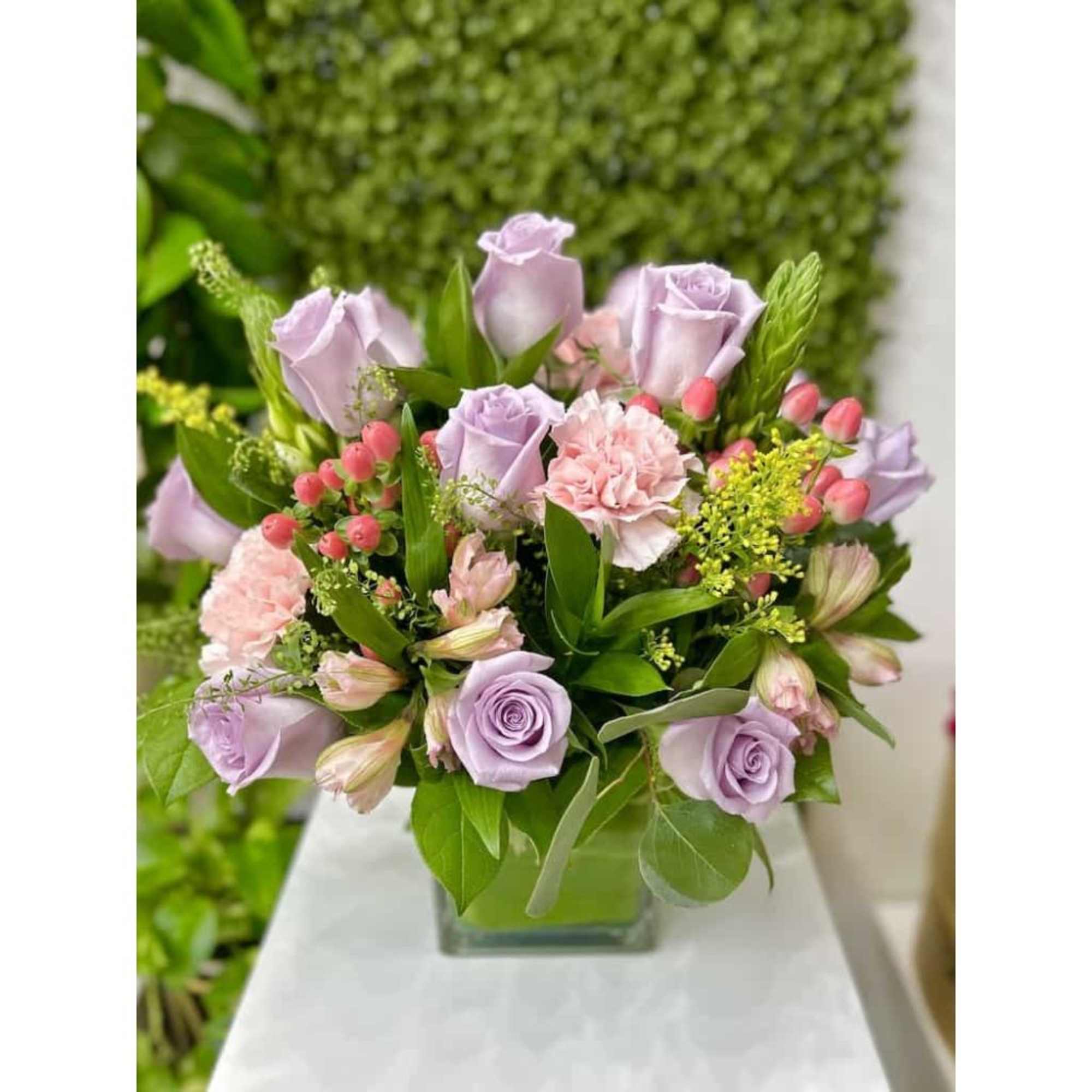 Lavender roses and pink carnations arranged in a clear glass cube vase.