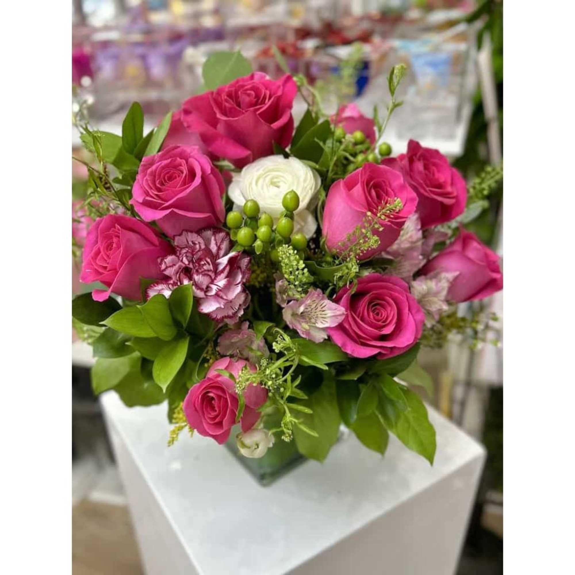 Arrangement of hot pink roses with pale pink blooms and white ranunculus in a green glass square vase