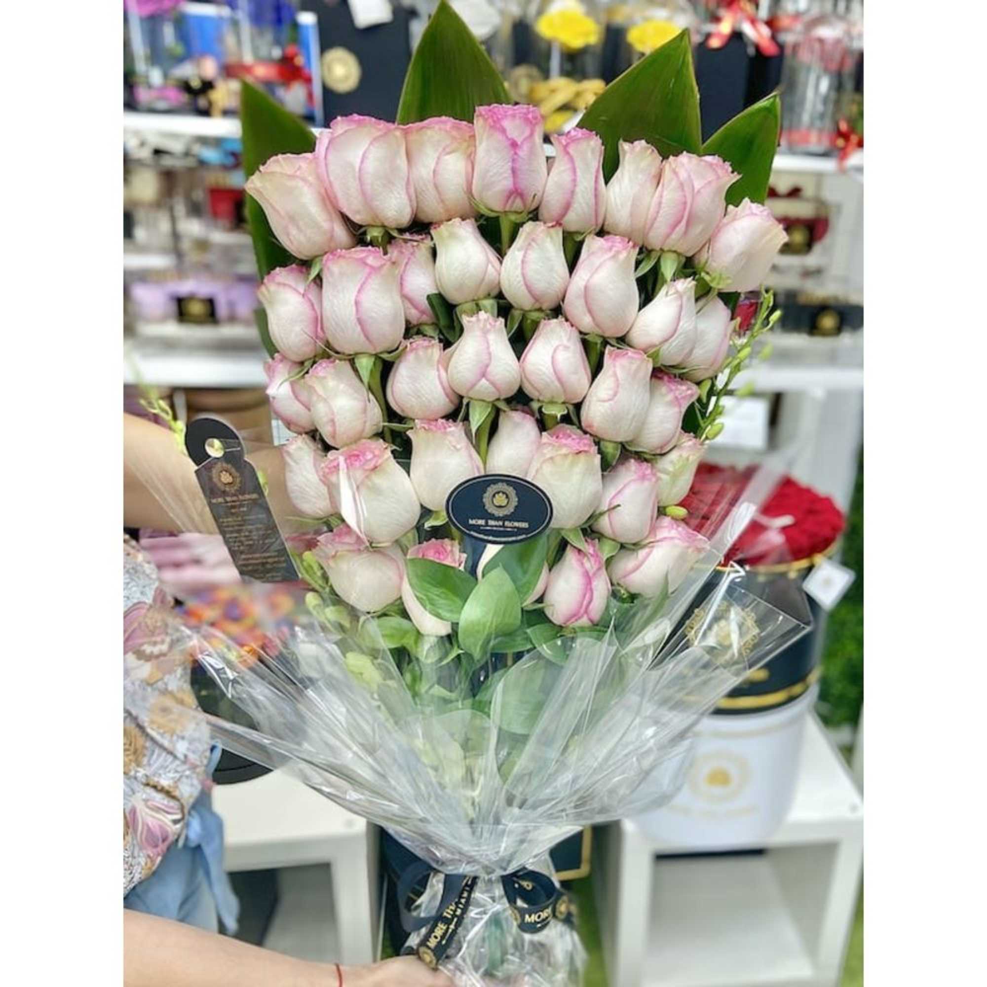 Tall bouquet of tightly clustered white roses with pink edges wrapped in clear cellophane