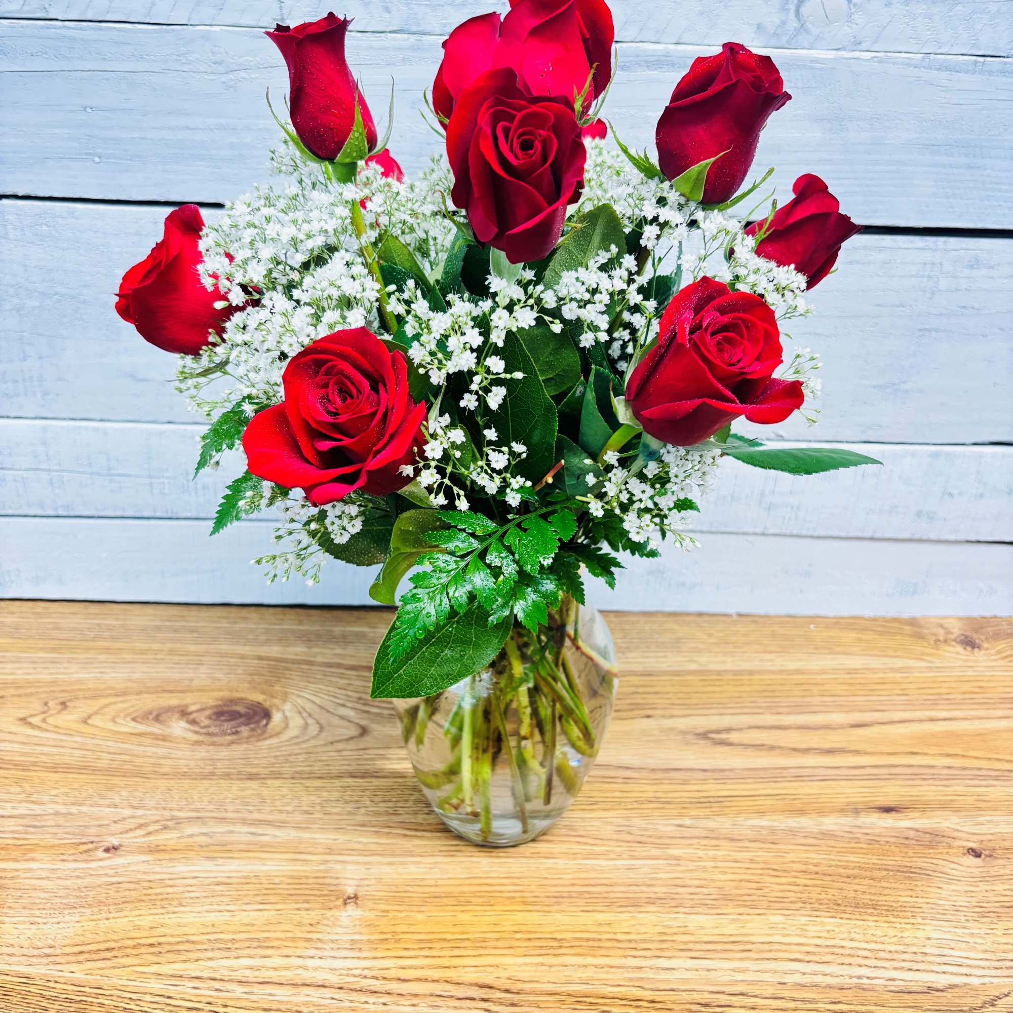Red roses arranged in a clear glass vase with white filler flowers