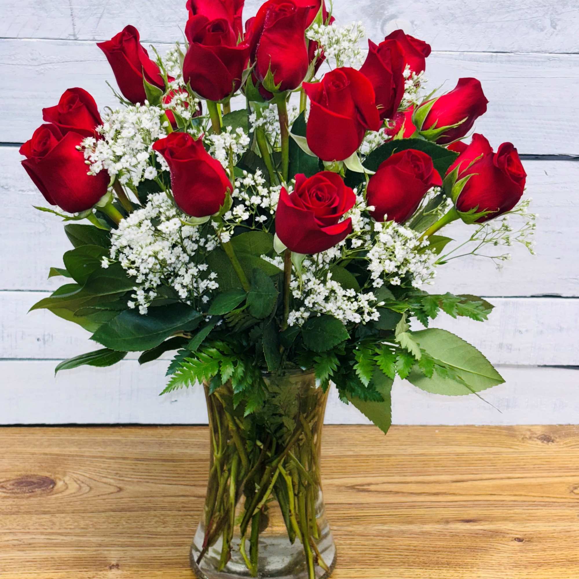 Red roses arranged in a clear glass vase with white filler flowers