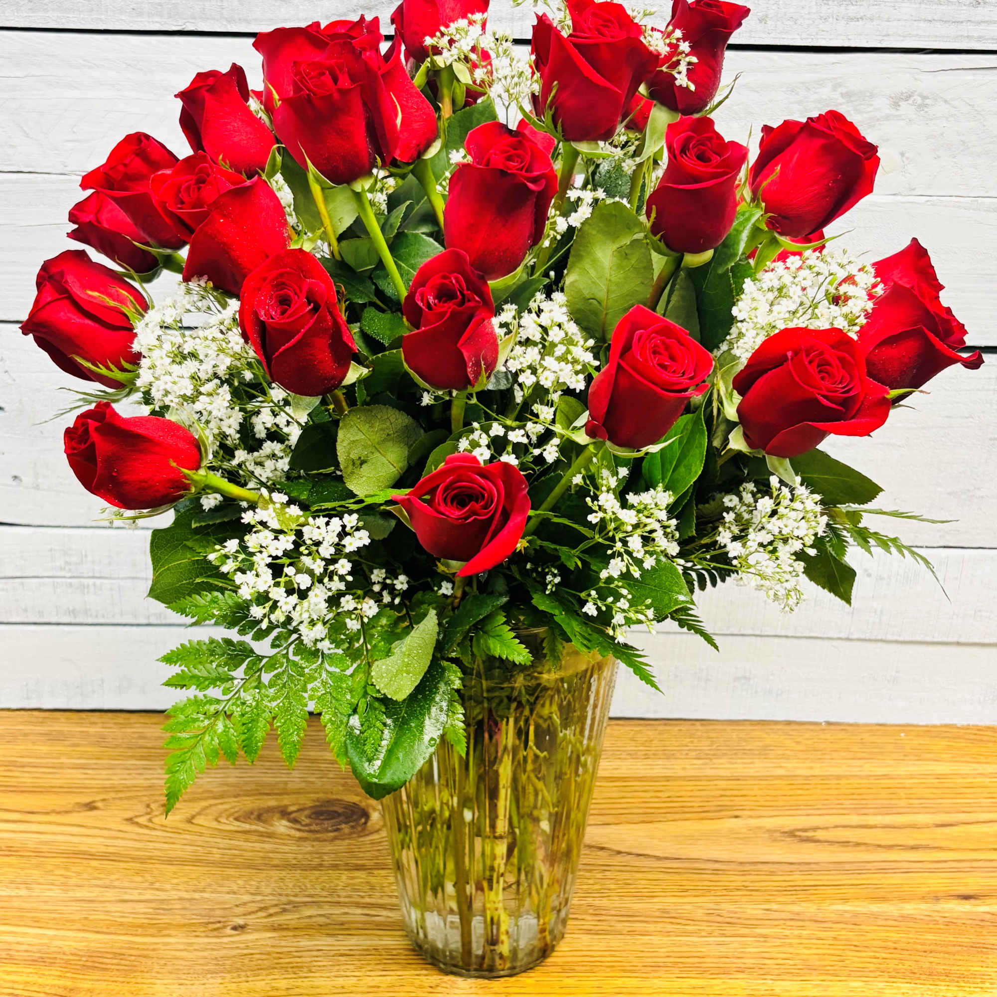 Red roses arranged in a clear glass vase with white filler flowers