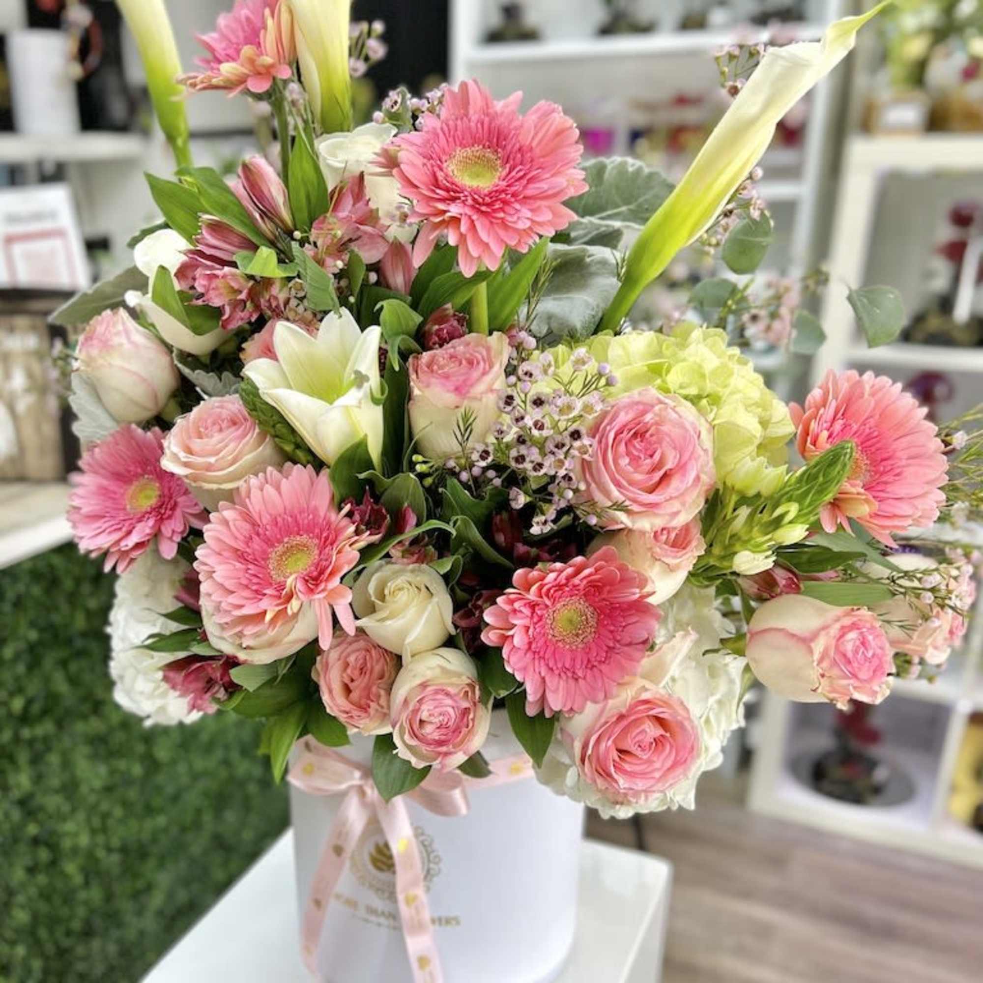 Pink and white flower arrangement with gerbera daisies, roses, and lilies in a white hatbox.