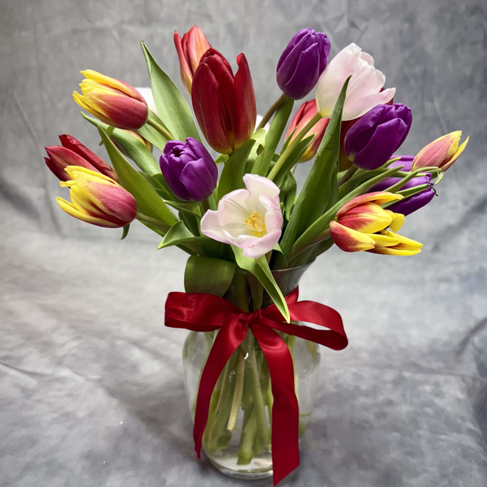Bouquet of multicolored tulips in a glass vase with a red ribbon