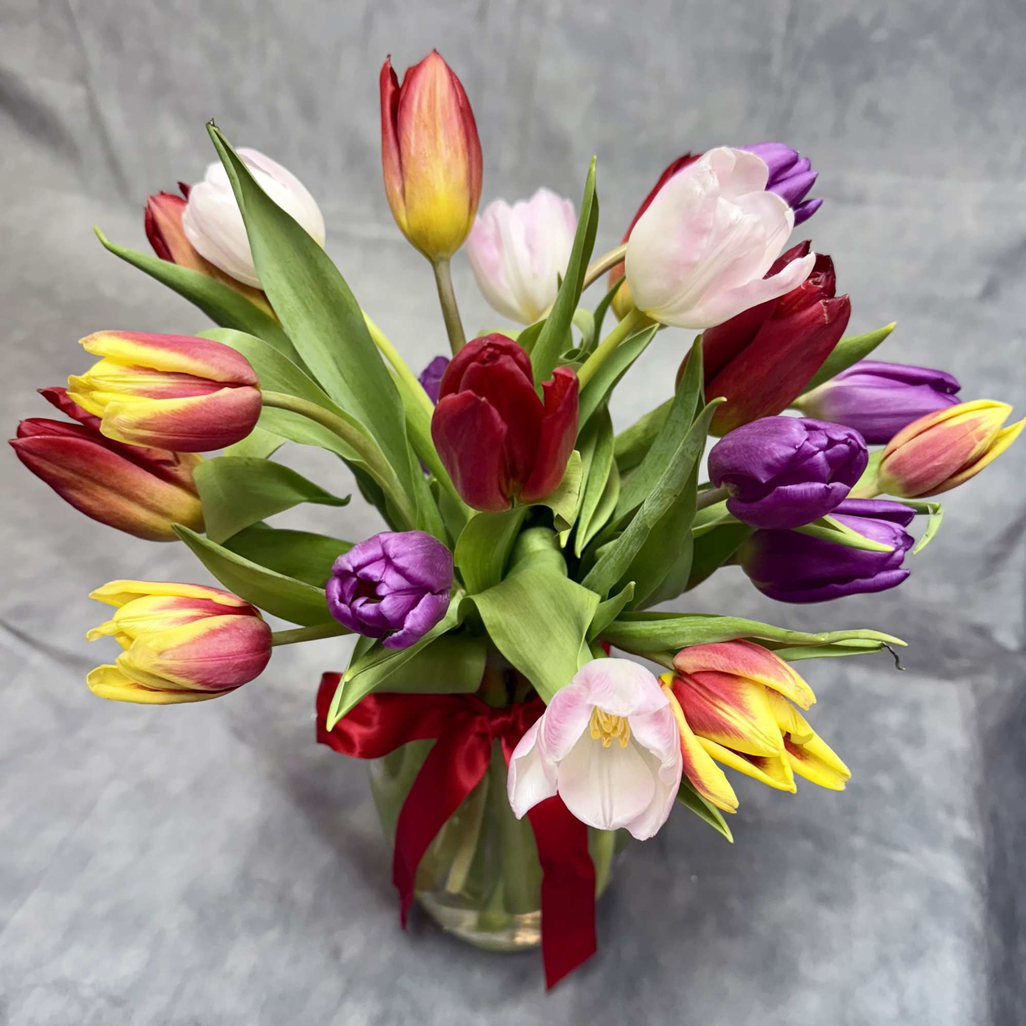 Bouquet of multicolored tulips in a glass vase with a red ribbon, photo 2 of 2