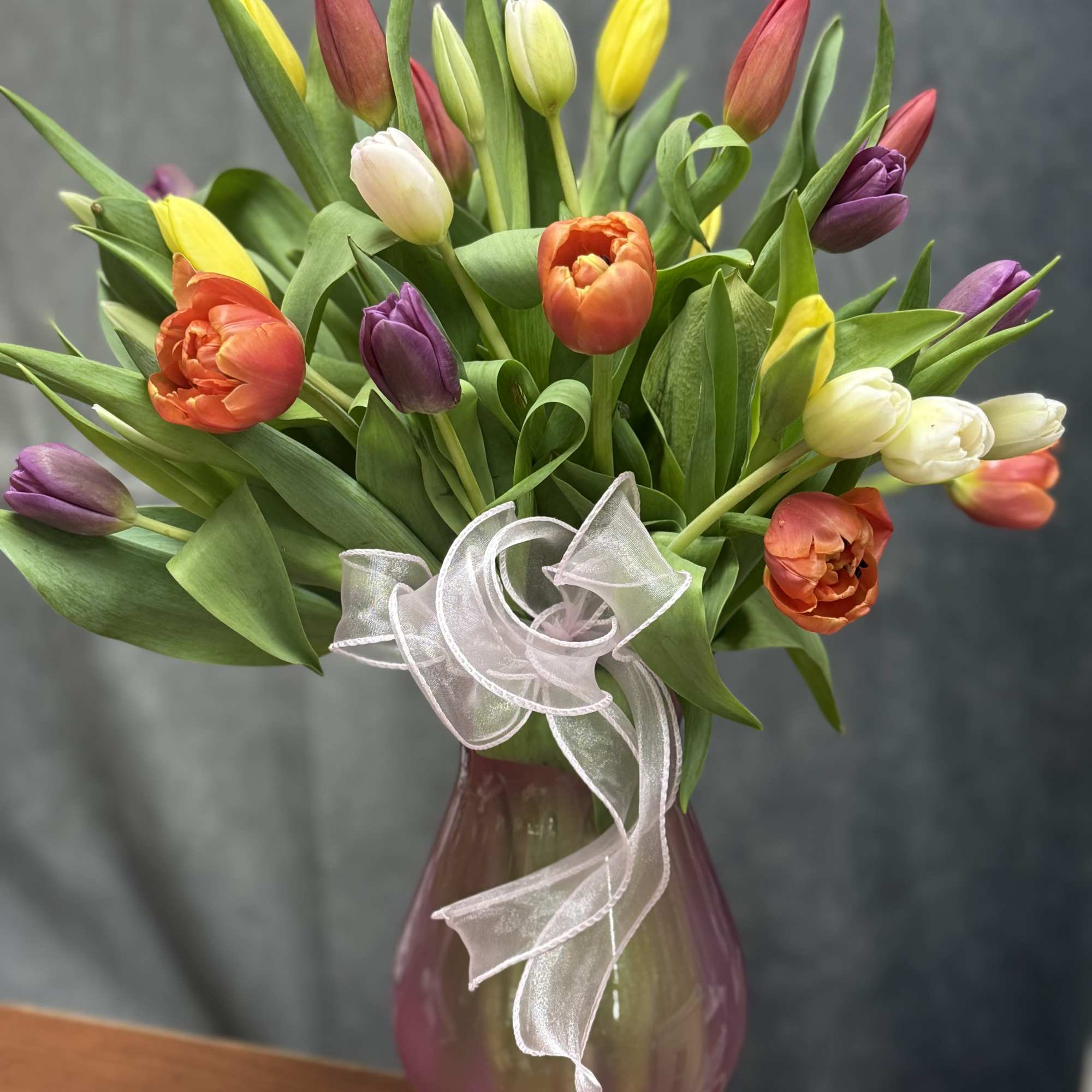 Colorful tulip bouquet in a purple glass vase with a sheer ribbon