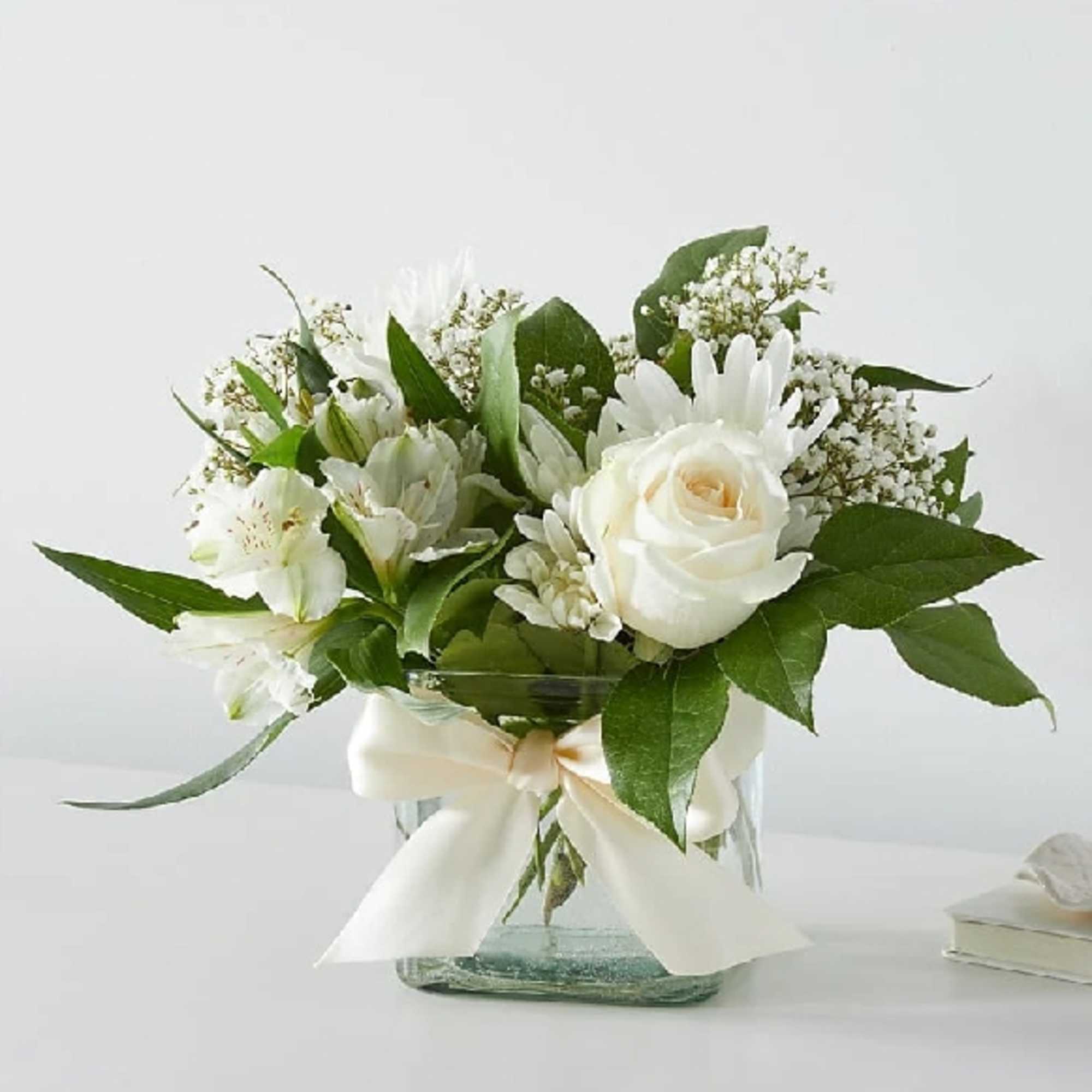 White rose and lily bouquet in a glass vase with a ribbon