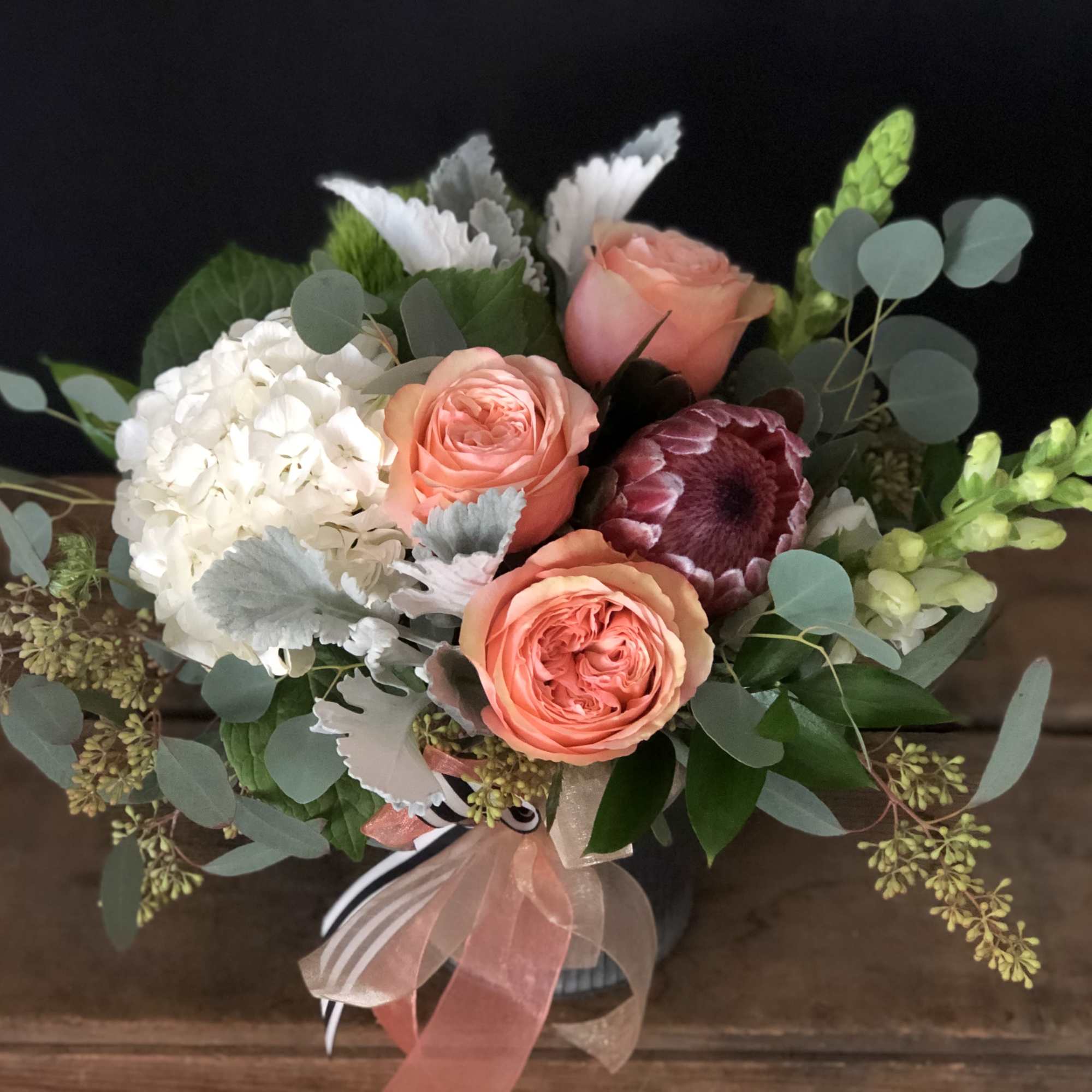 Bouquet of peach roses, white hydrangea, and mixed greenery in a vase