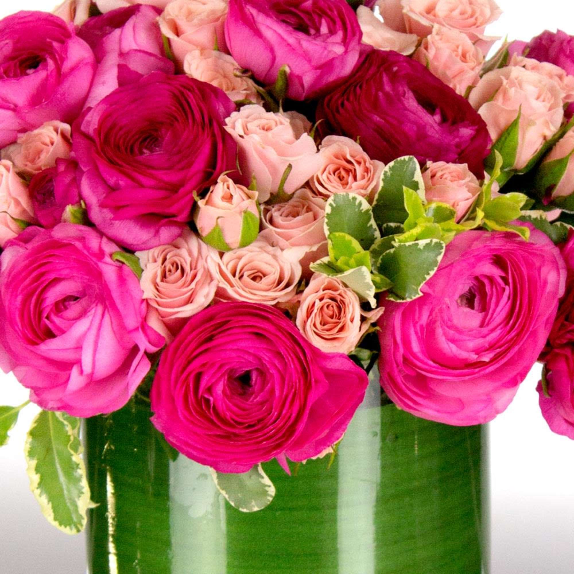 Pink ranunculus and blush roses arranged in a green glass vase