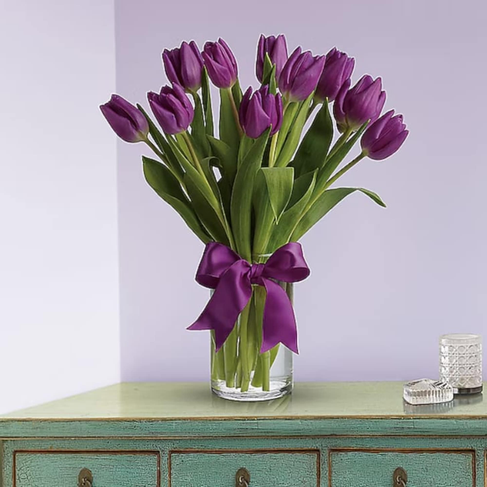 Tall bunch of purple tulips in a clear glass vase tied with a purple ribbon