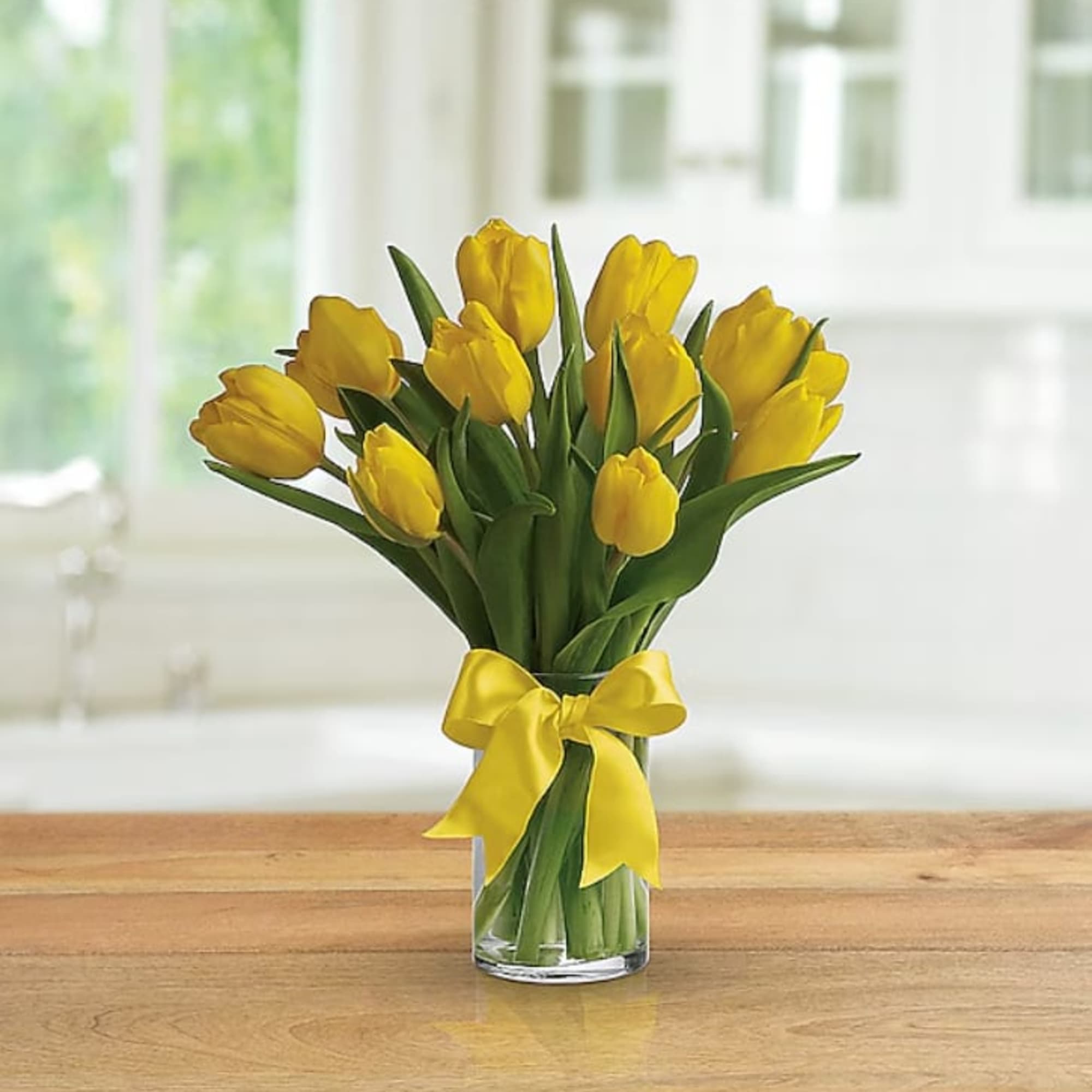 Clear vase of yellow tulips with a yellow bow on a wooden table