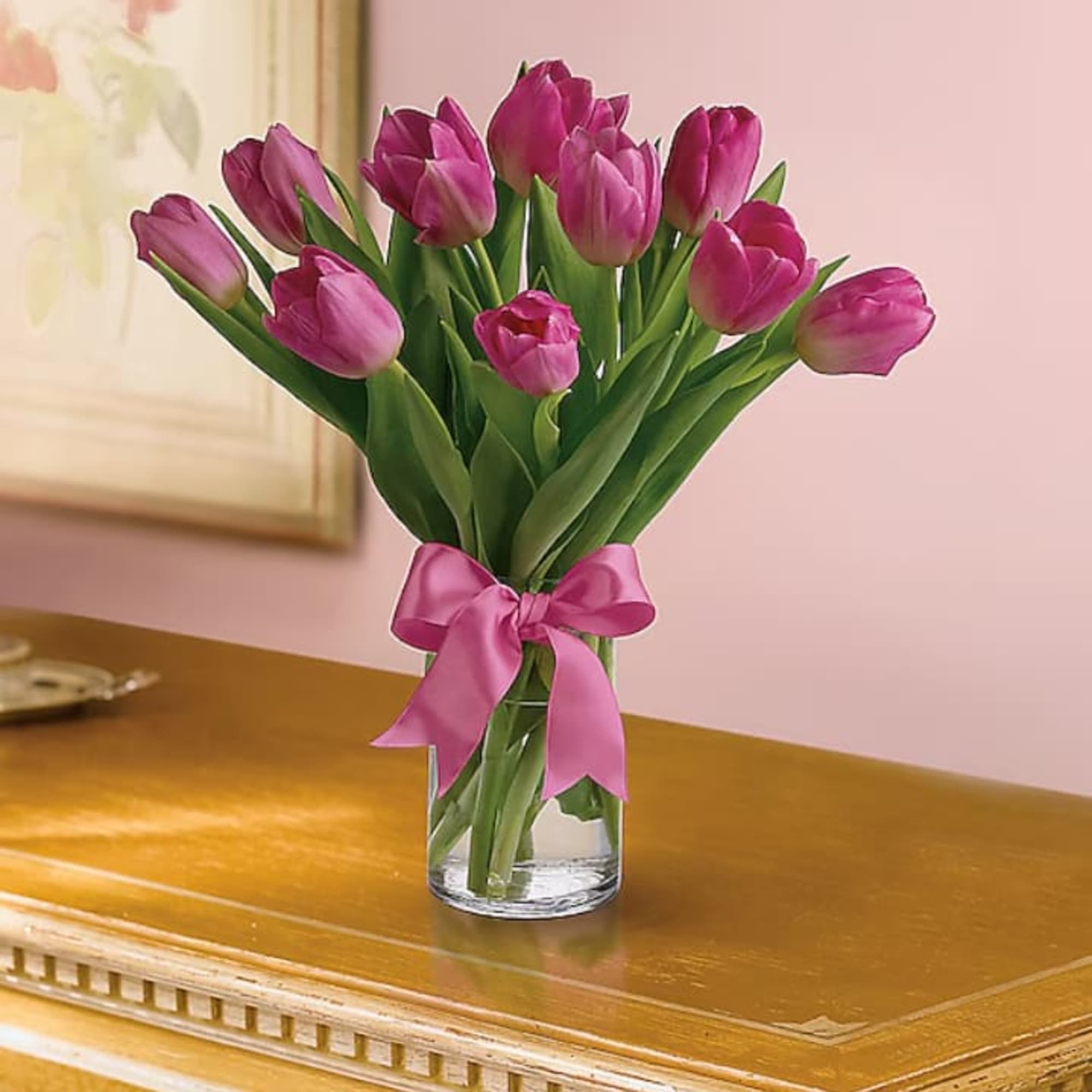 Pink tulips arranged in a clear glass vase with a matching pink bow on a wooden table