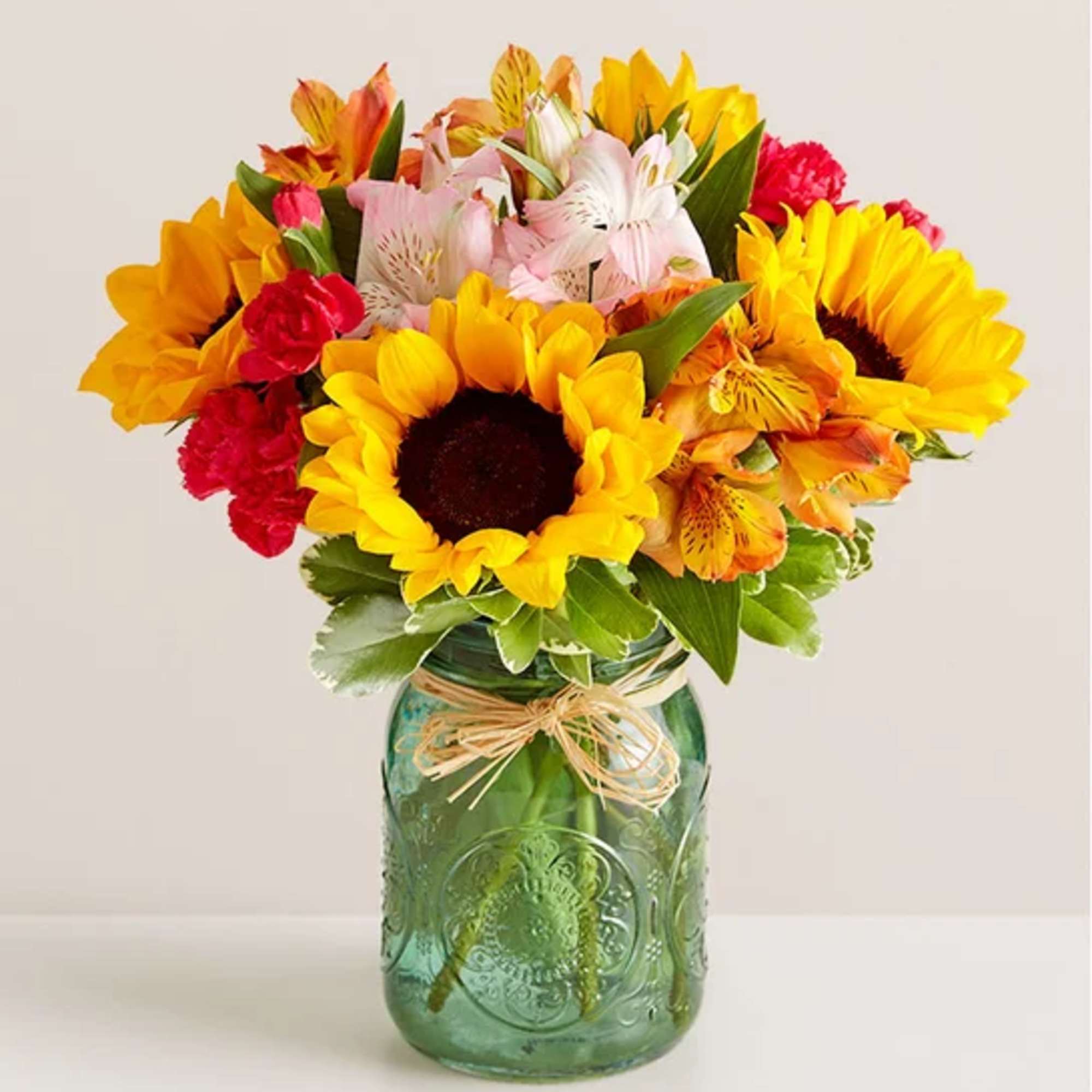 Bouquet of sunflowers, alstroemeria, and carnations in a green glass jar