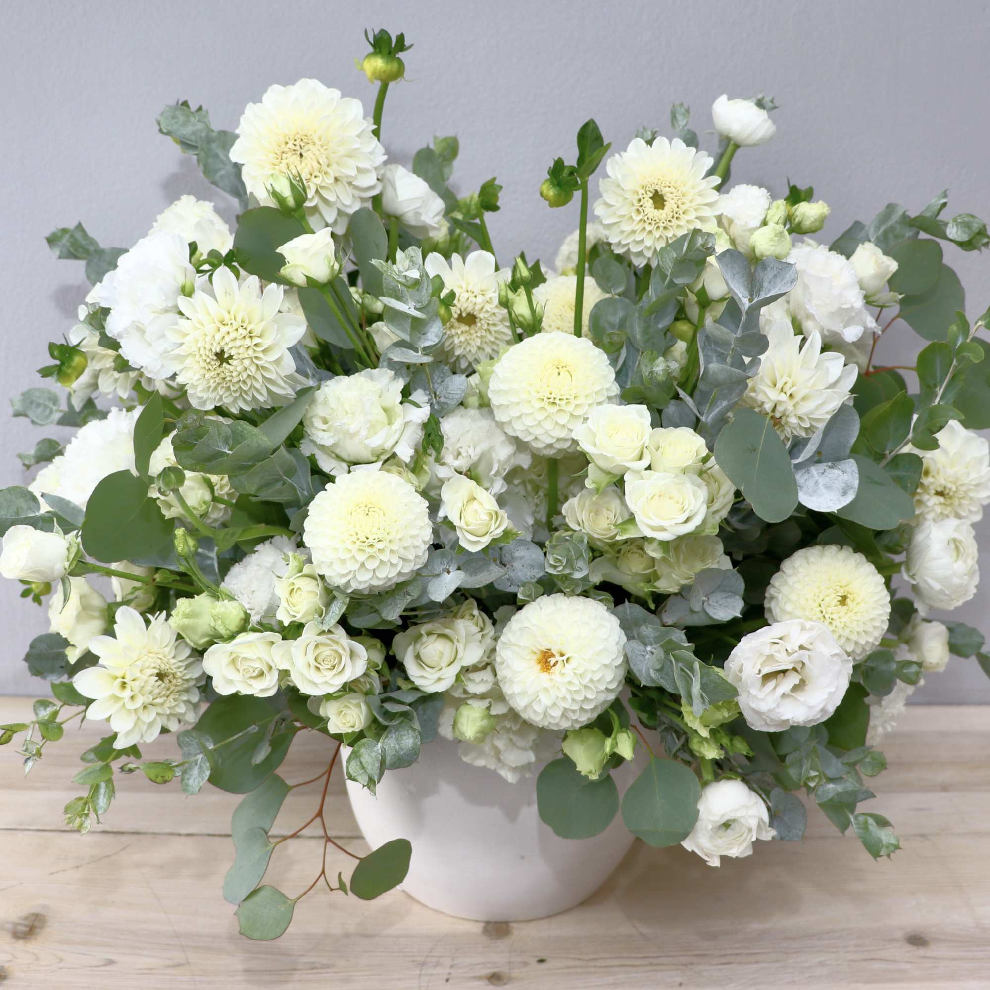 White flowers arranged in a white vase with soft green foliage