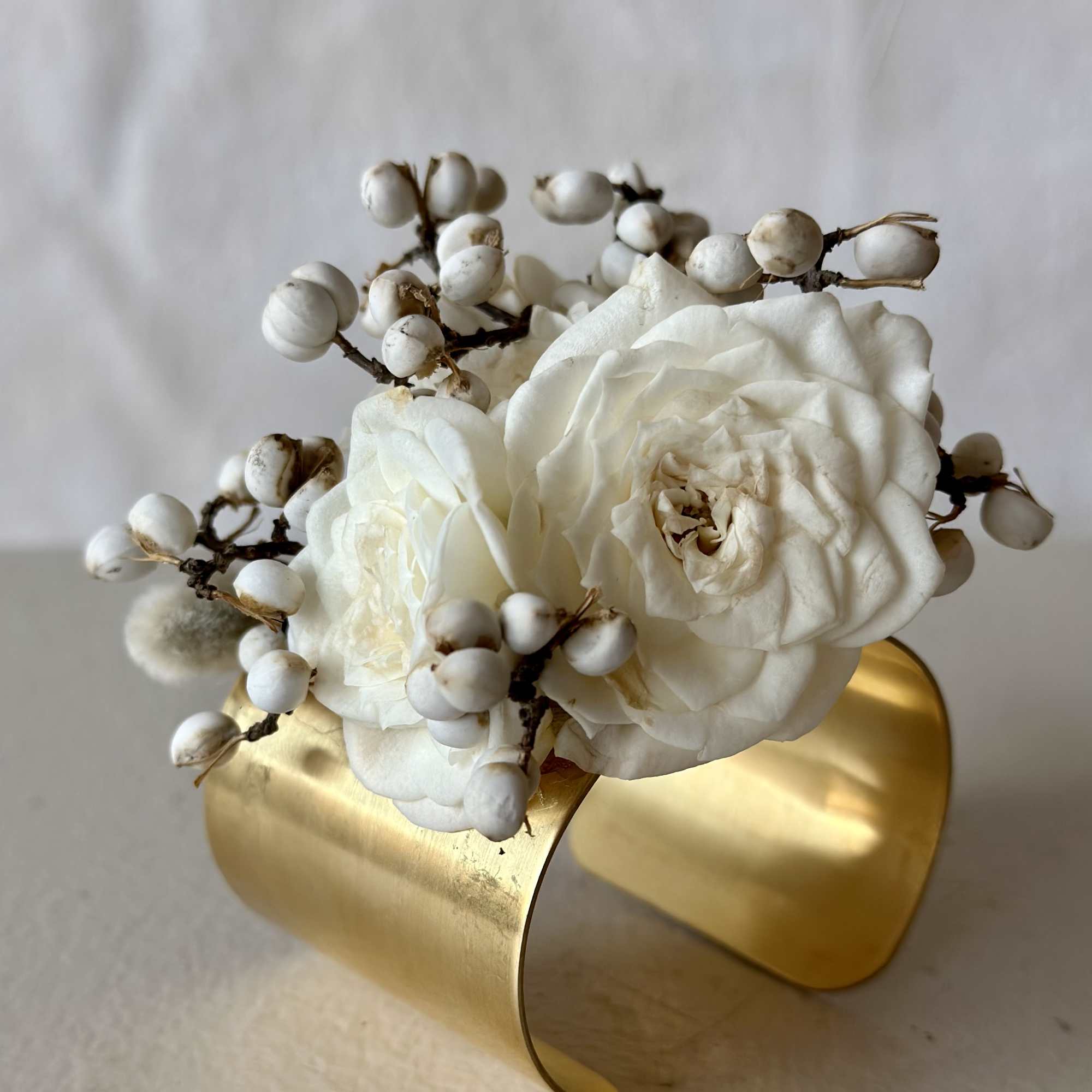 White roses with berry sprigs in a gold cuff vase