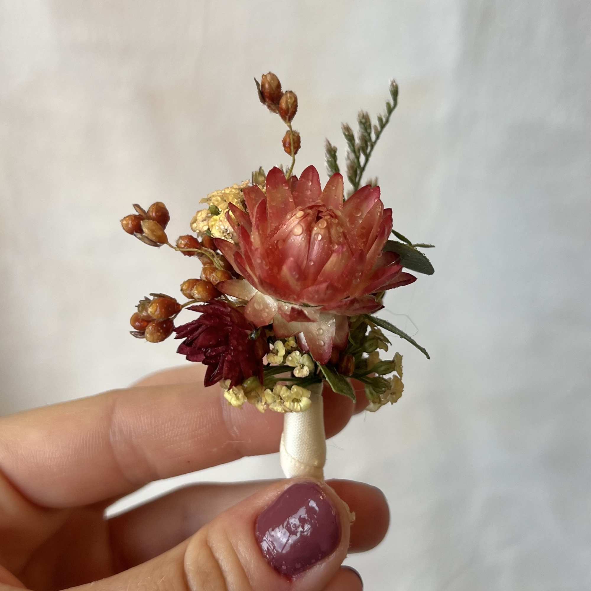Small boutonniere with red and pink flowers held between fingers