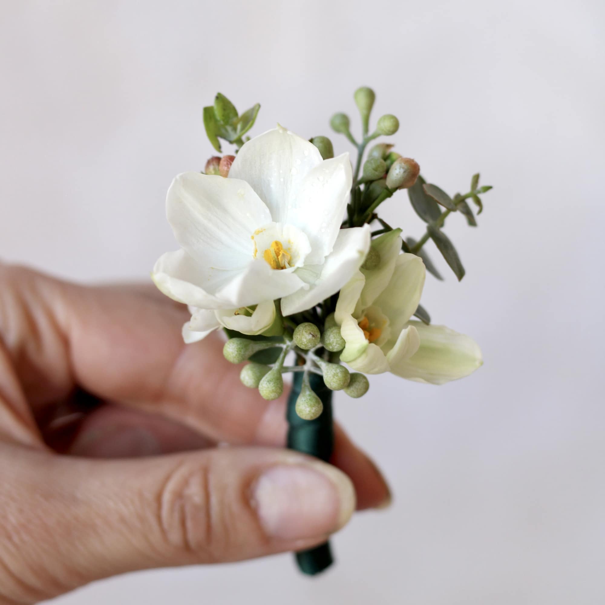 White boutonniere with small green accents held in a hand