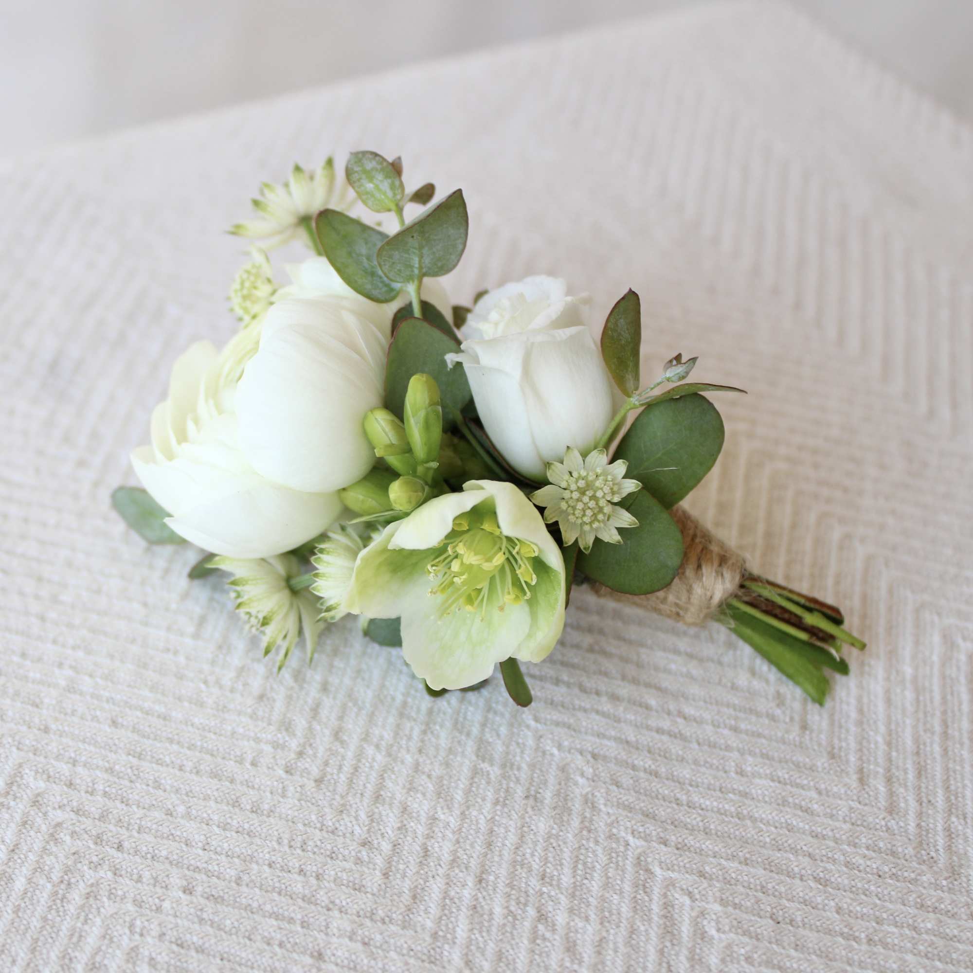 Small white boutonniere with green foliage on a beige fabric background