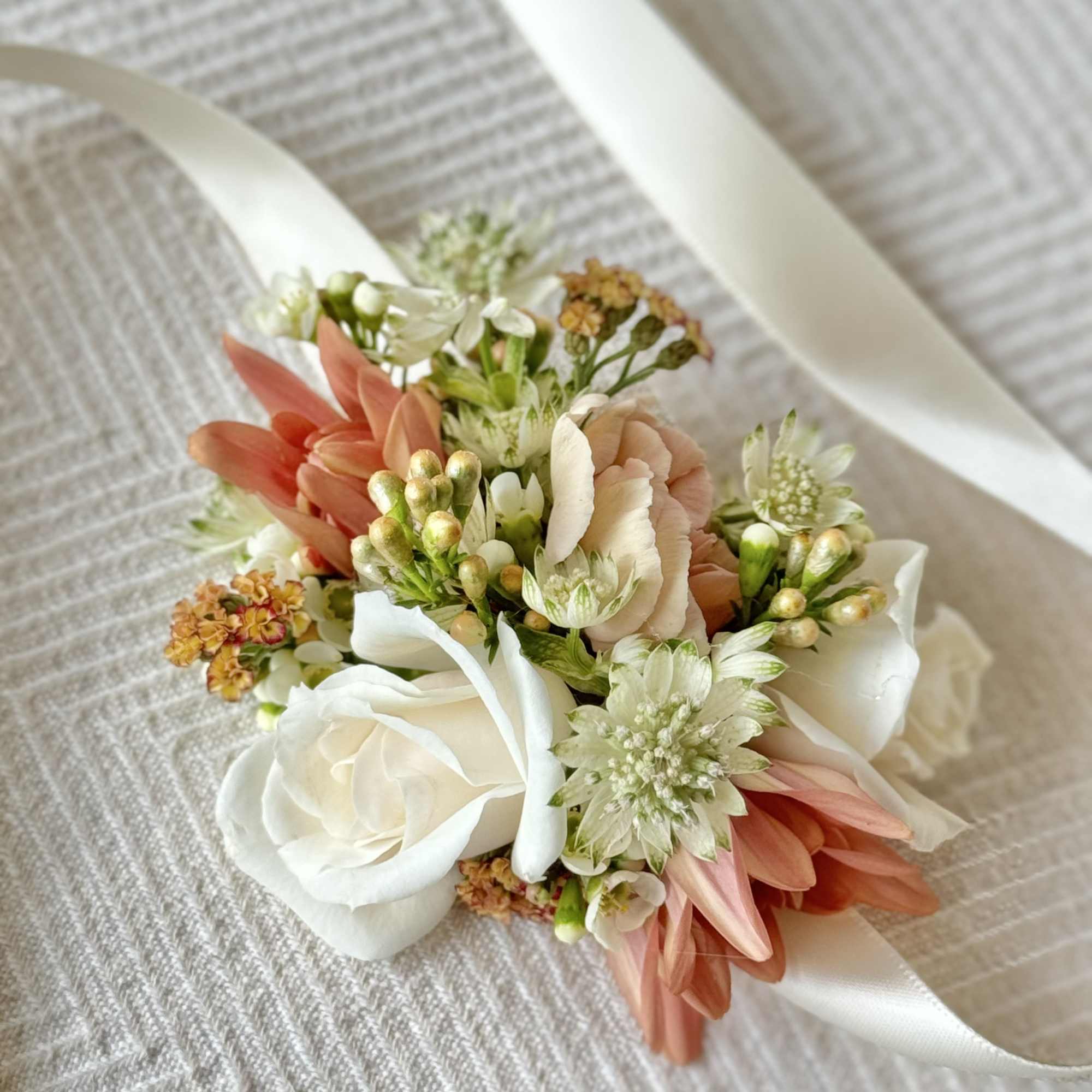 Small wrist corsage with white and peach flowers on a satin ribbon