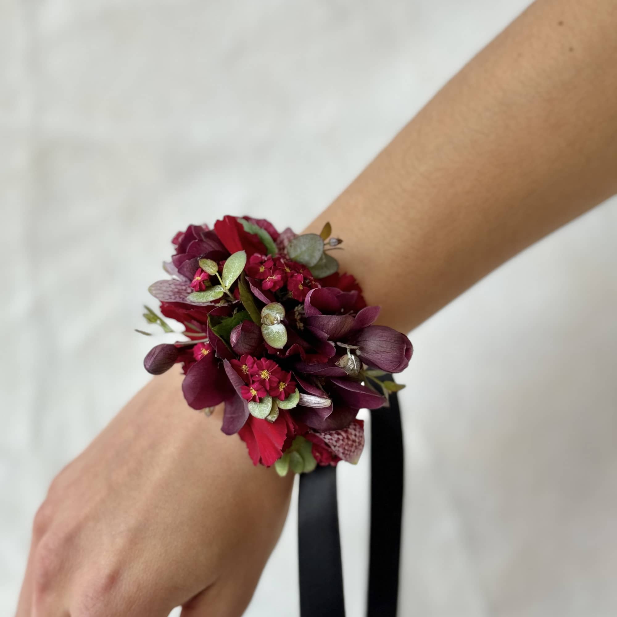 Dark burgundy wrist corsage with small flowers and ribbon