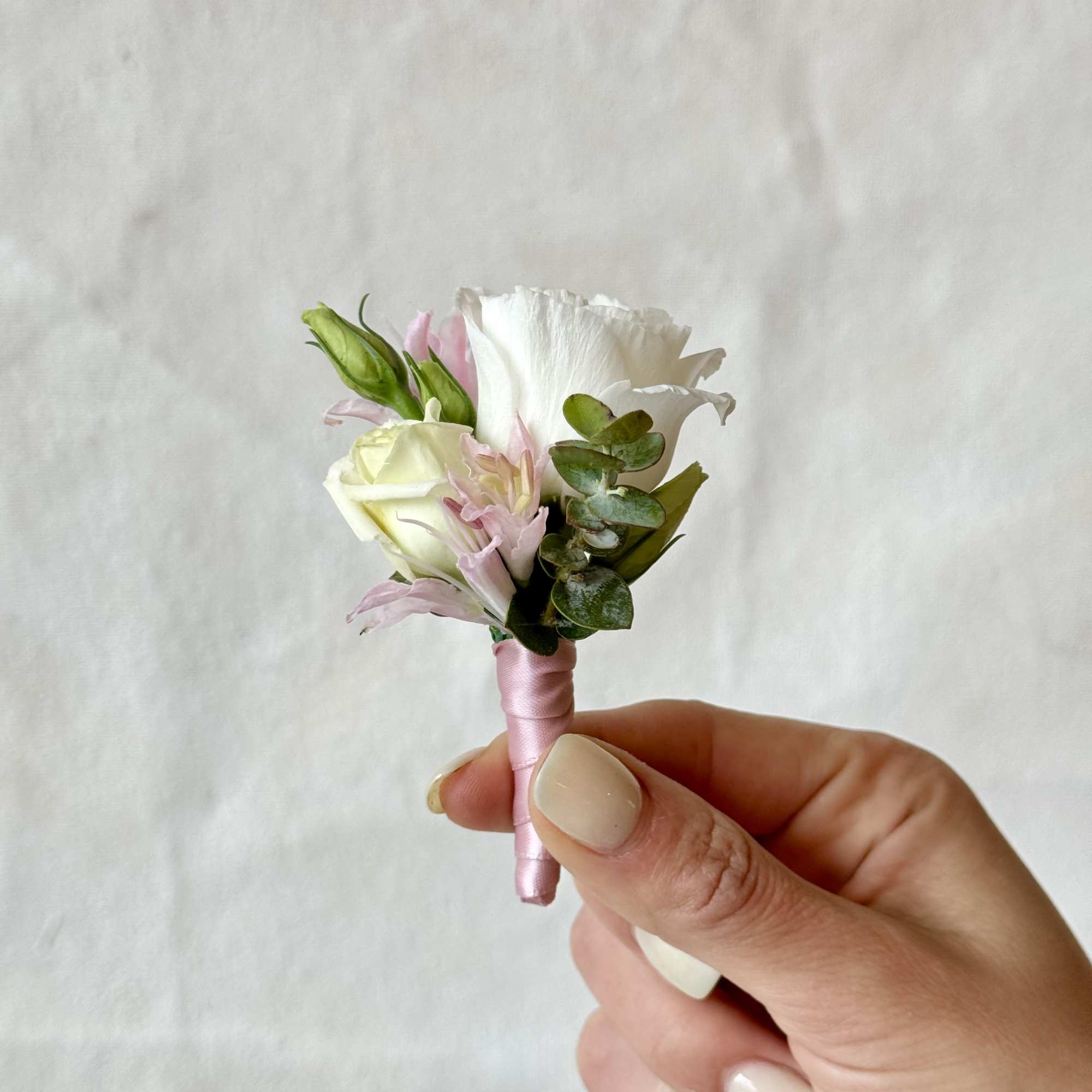 Small pink and white boutonniere with ribbon wrap held in a hand