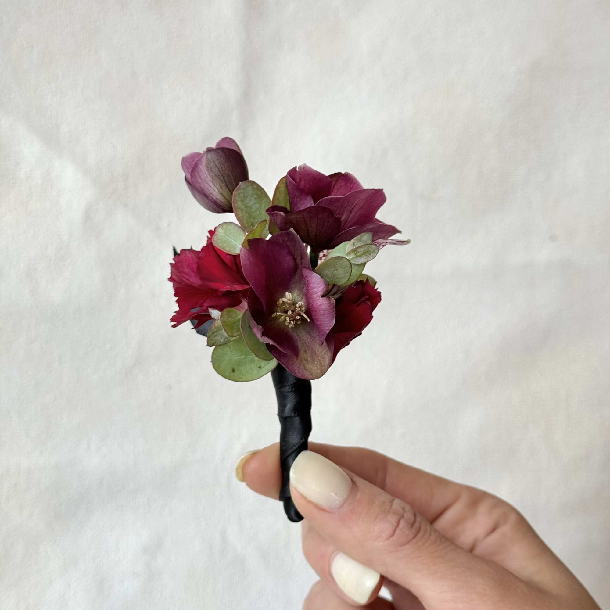 Small burgundy boutonniere with dark petals and round green leaves