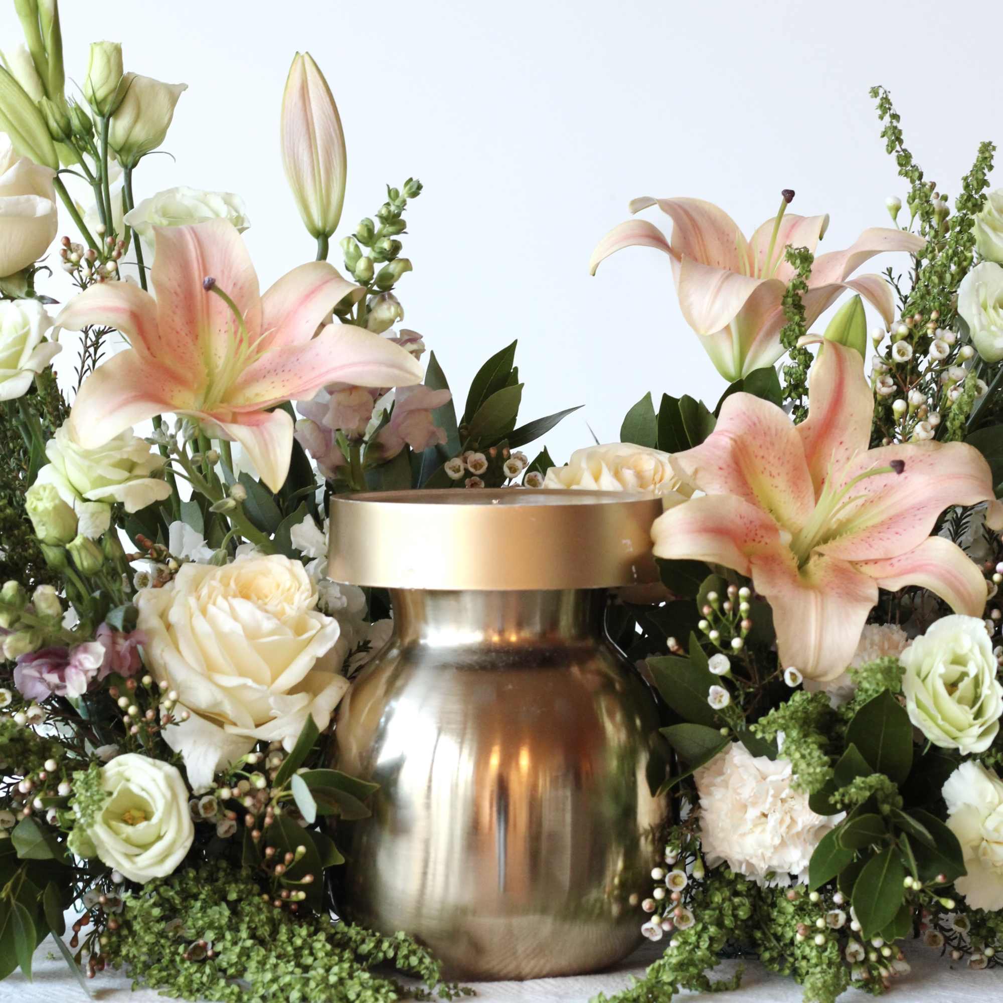 Floral arrangement with pink lilies and cream roses around a gold urn