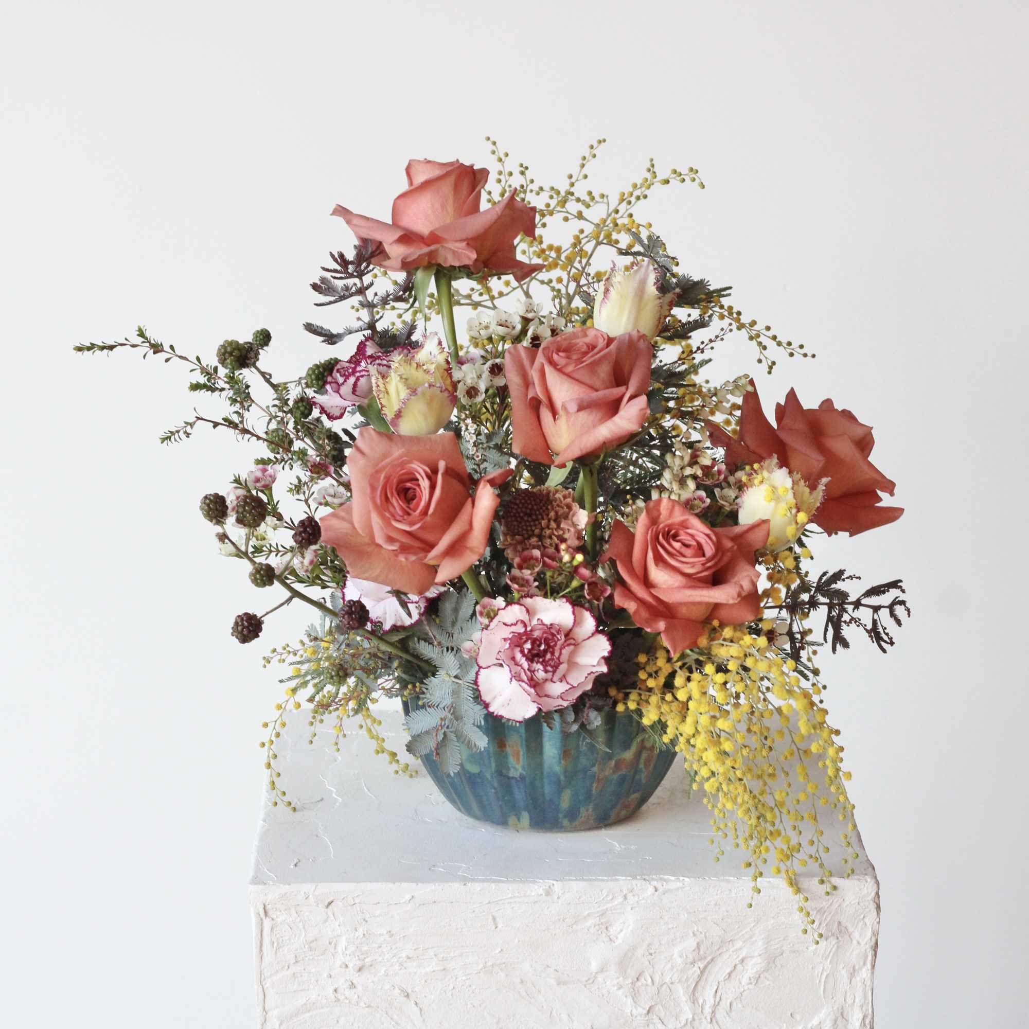 Peach rose and pink carnation arrangement with yellow accents in a blue-green ceramic bowl