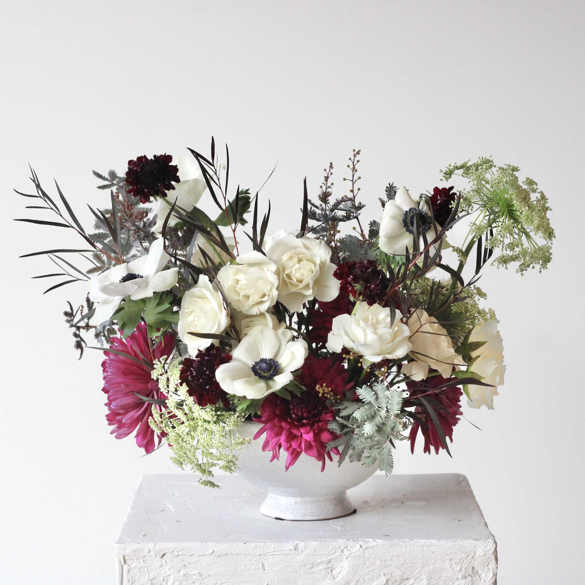 Mixed floral arrangement in a white pedestal vase with white and burgundy blooms