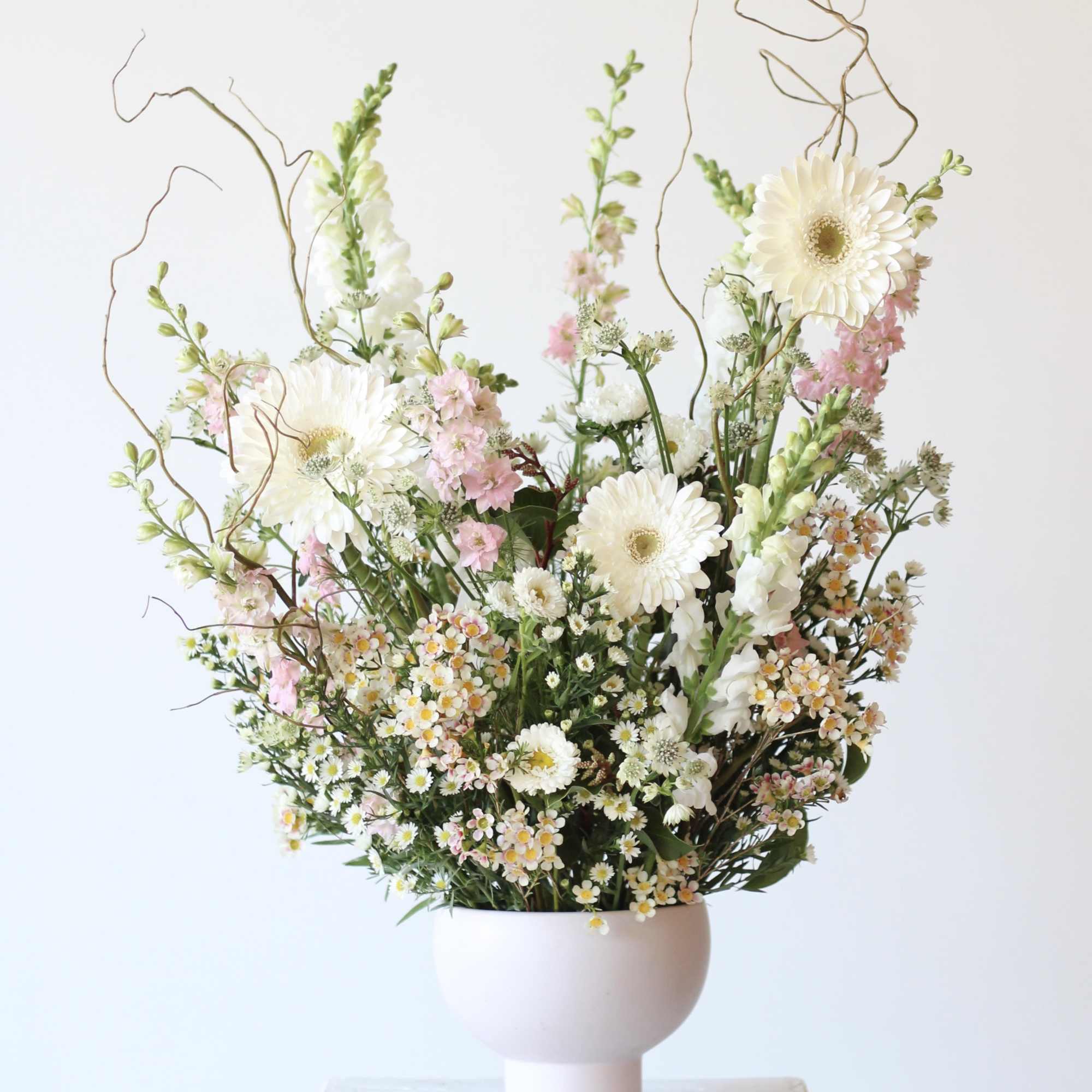 Tall bouquet of white and pink flowers in a pale vase