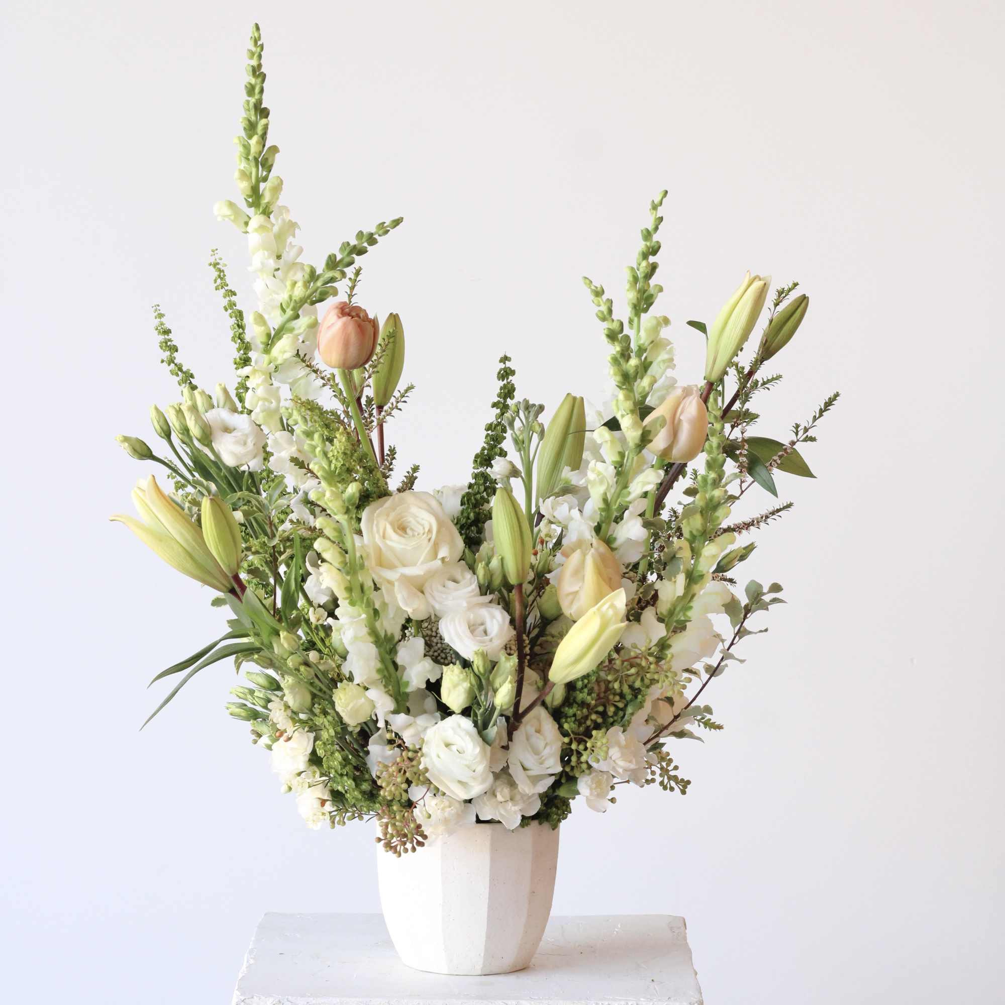 Tall white floral arrangement with lilies, roses, and snapdragons in a white vase