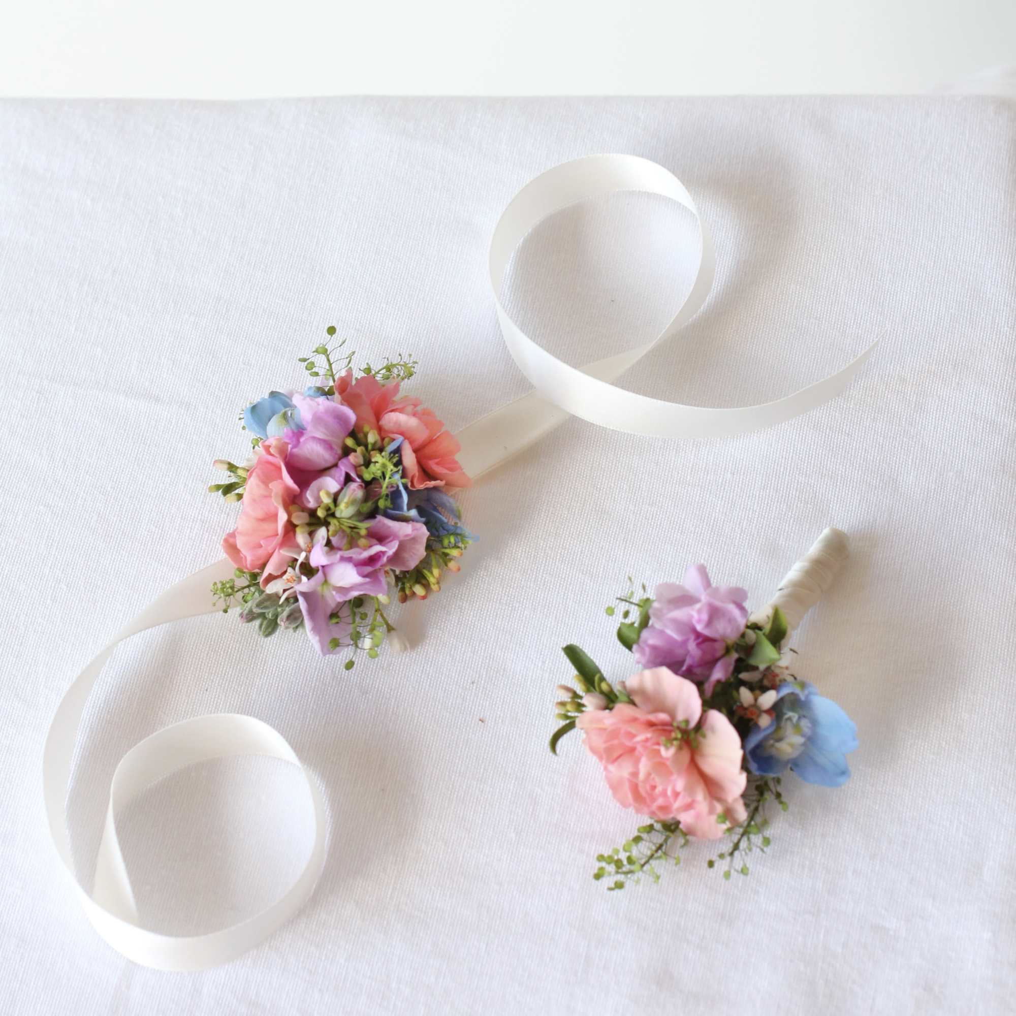Two small pastel floral boutonnieres with white ribbon loops
