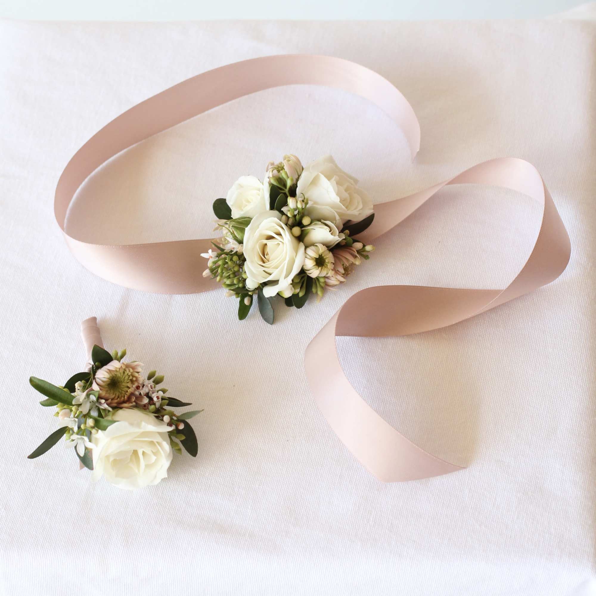 Two white floral wrist corsages with pale pink ribbon