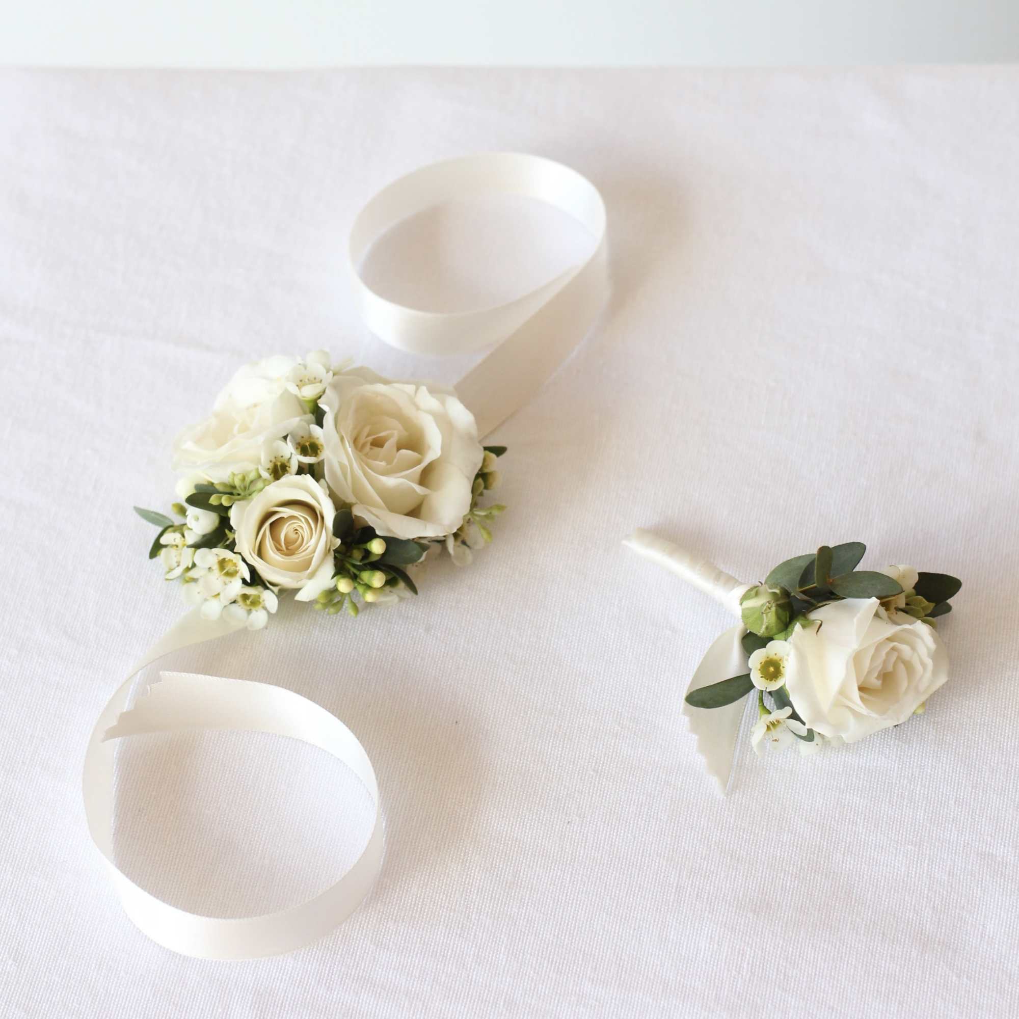 White rose corsages with ribbon ties on a white cloth