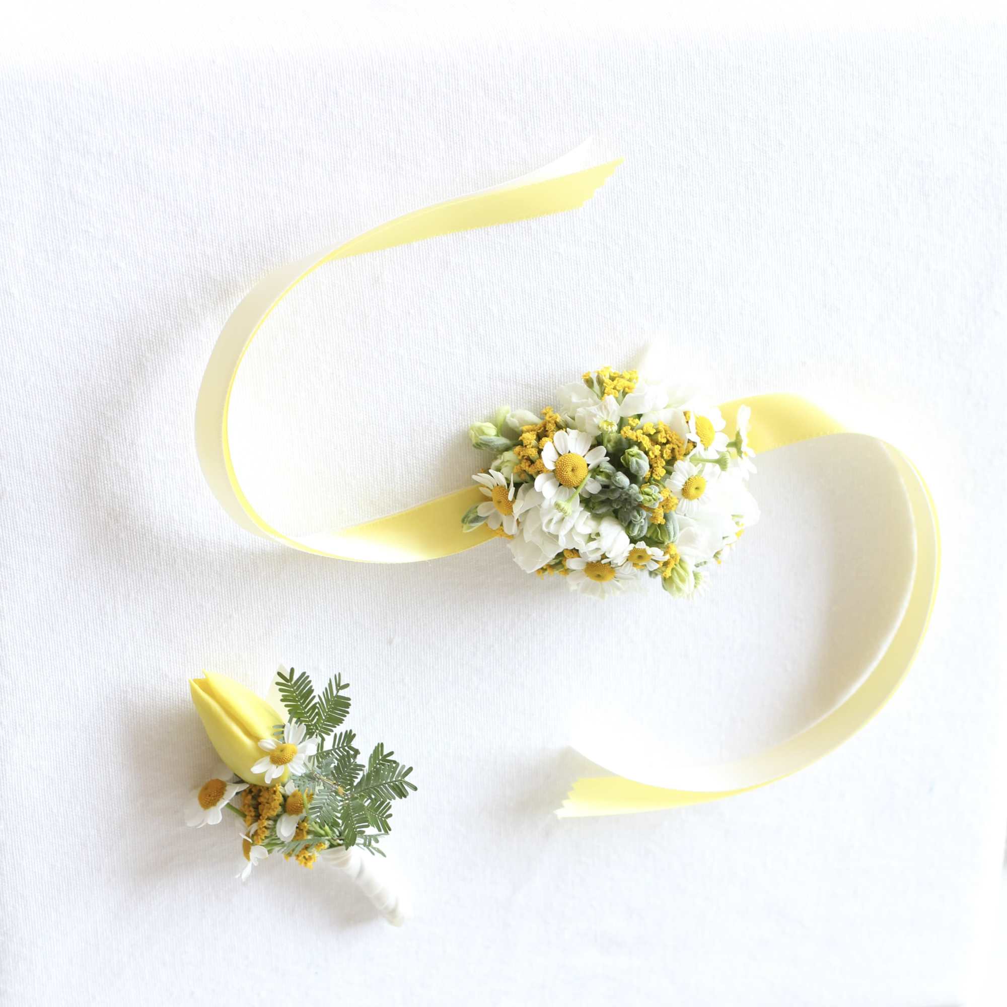 Two small floral wrist corsages with yellow ribbon on a white background