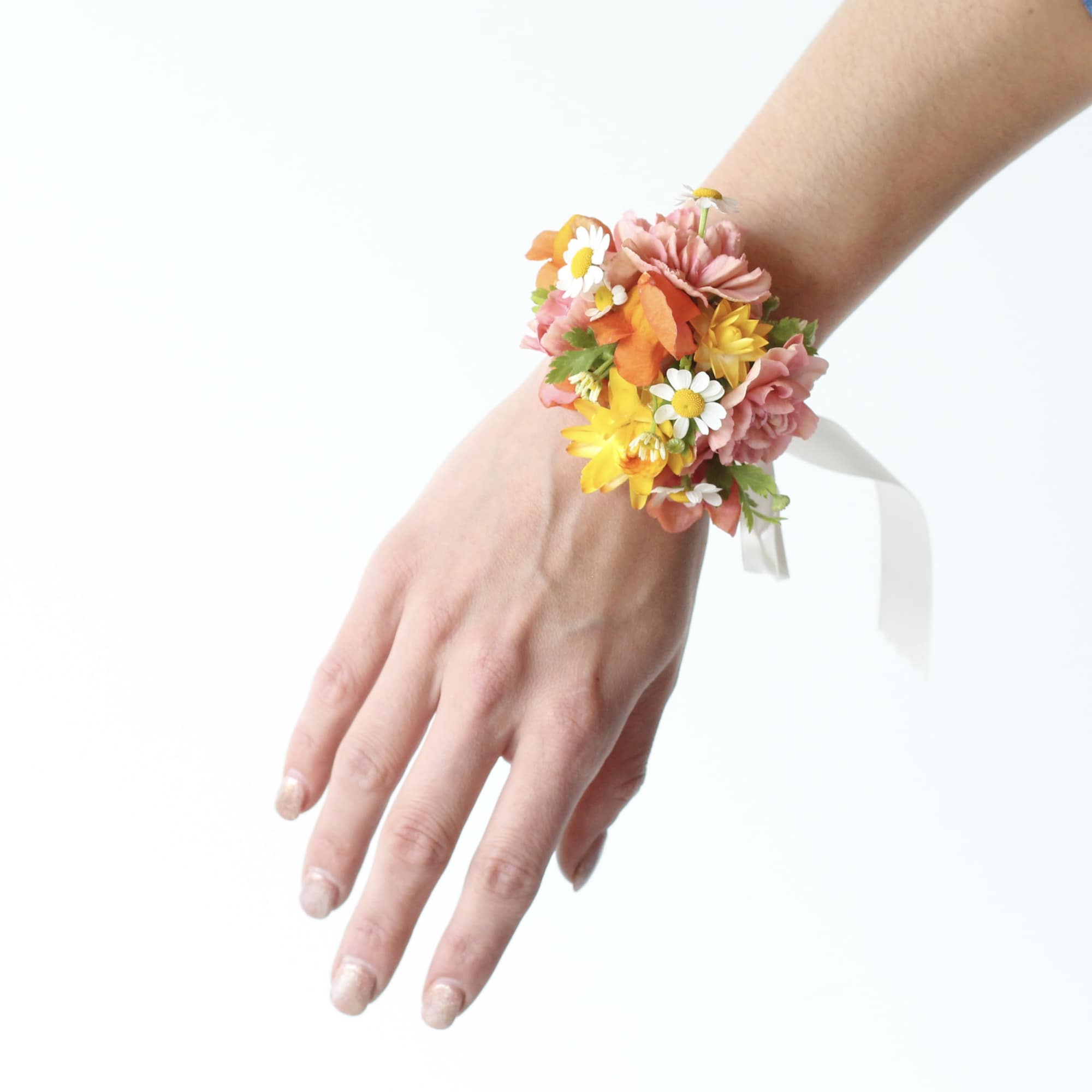 Floral wrist corsage with pink, yellow, and orange flowers on a white ribbon