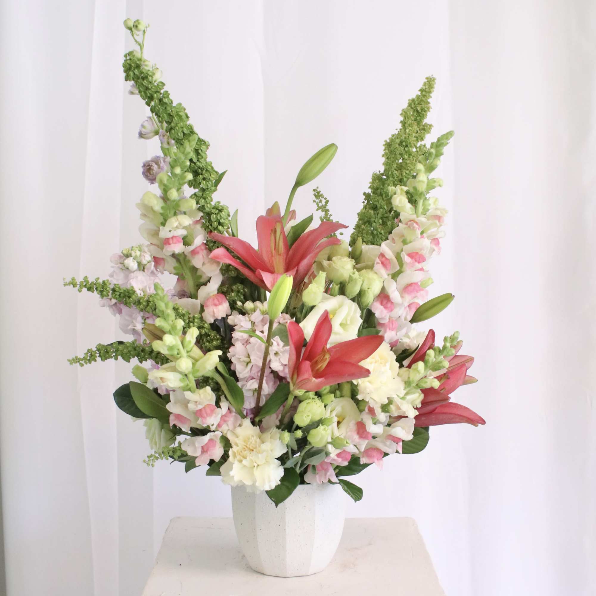Tall floral arrangement with pink lilies and white snapdragons in a white vase