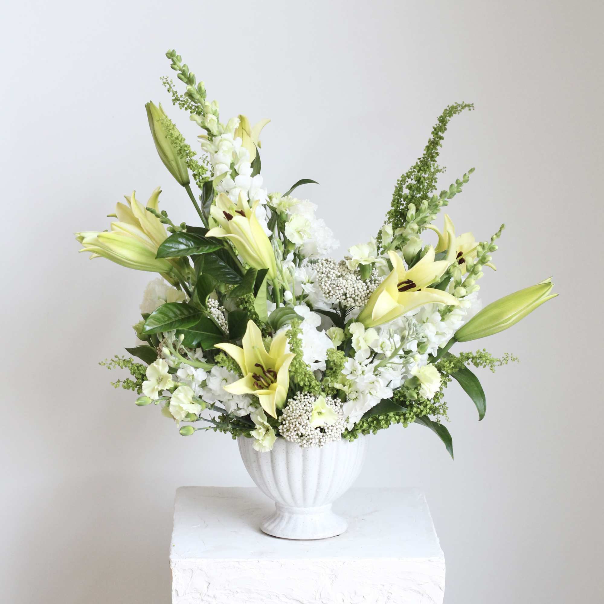 White and pale yellow lily arrangement in a white vase