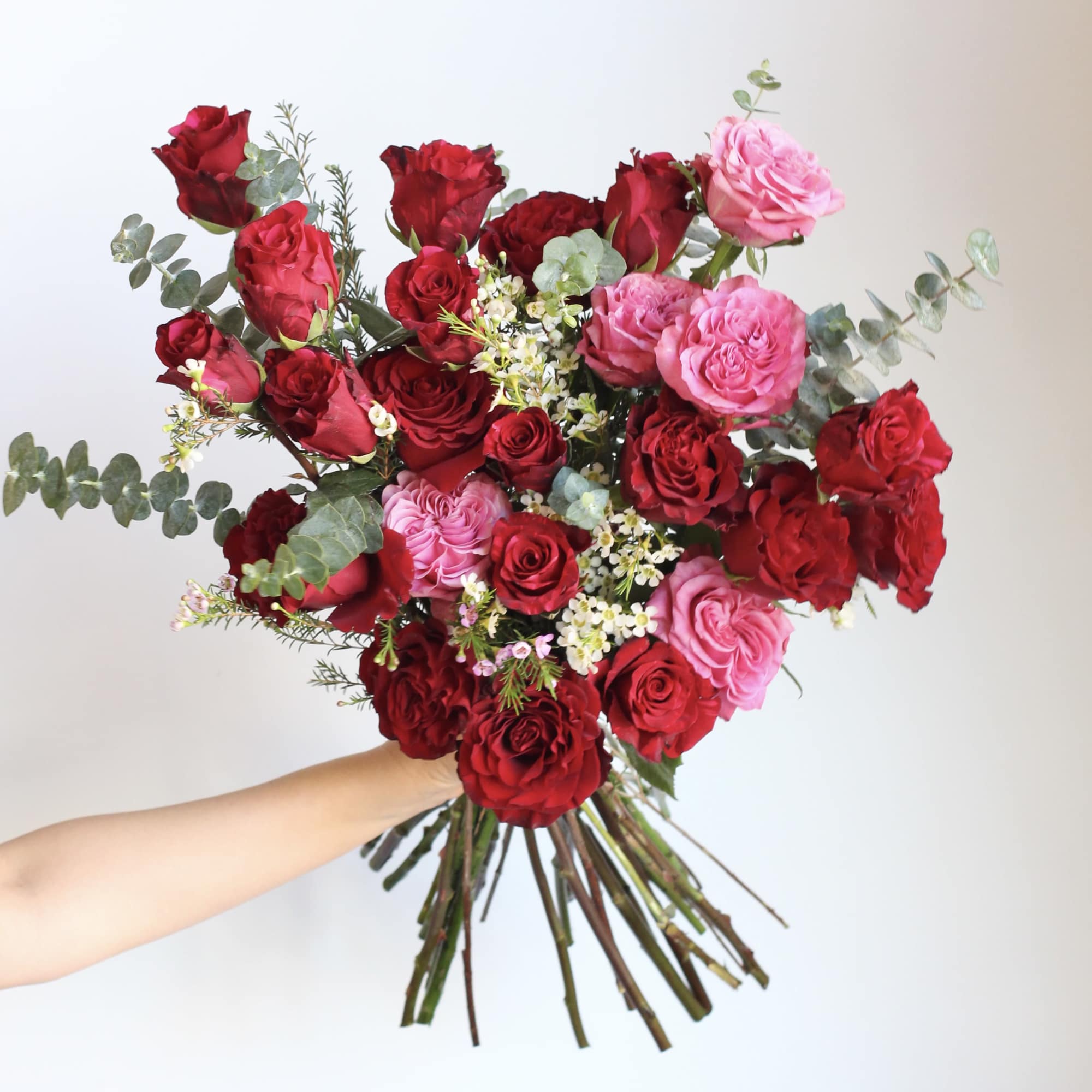 Handheld bouquet of red and pink roses with eucalyptus