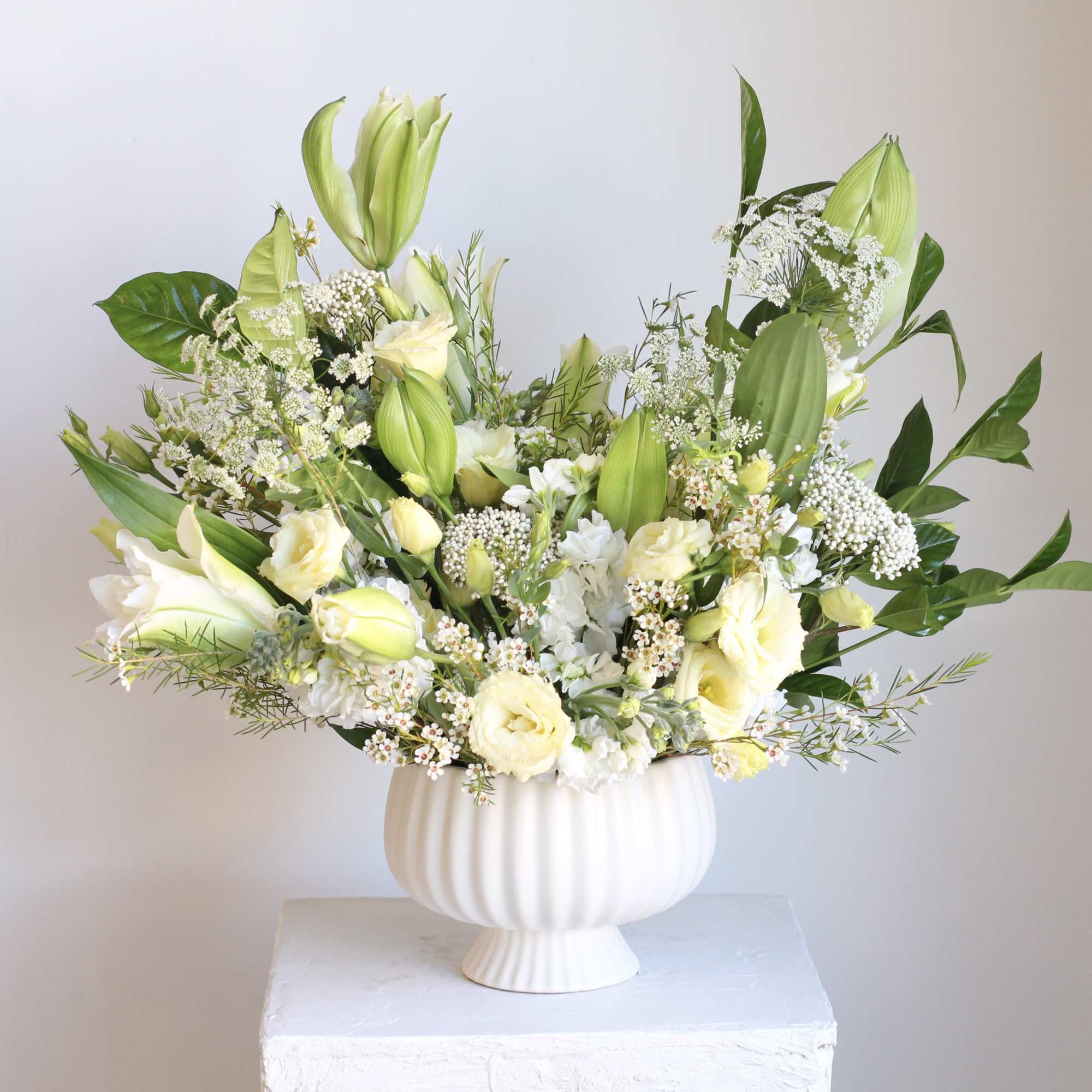 White and pale yellow floral arrangement in a white pedestal vase