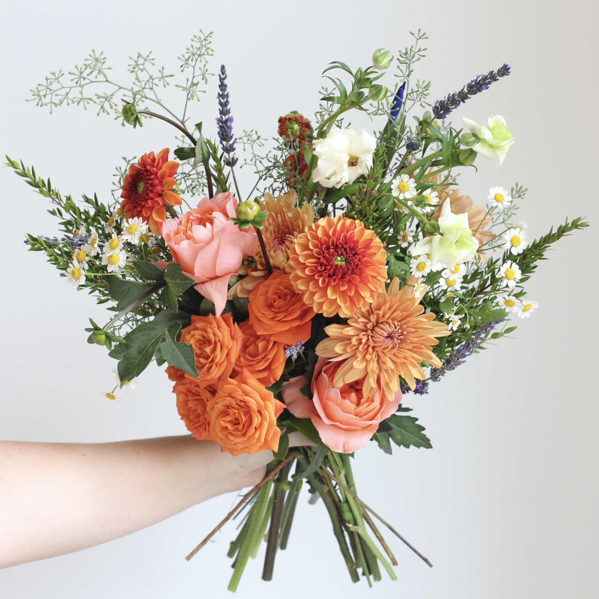 Handheld bouquet of orange and pink flowers with small white daisies