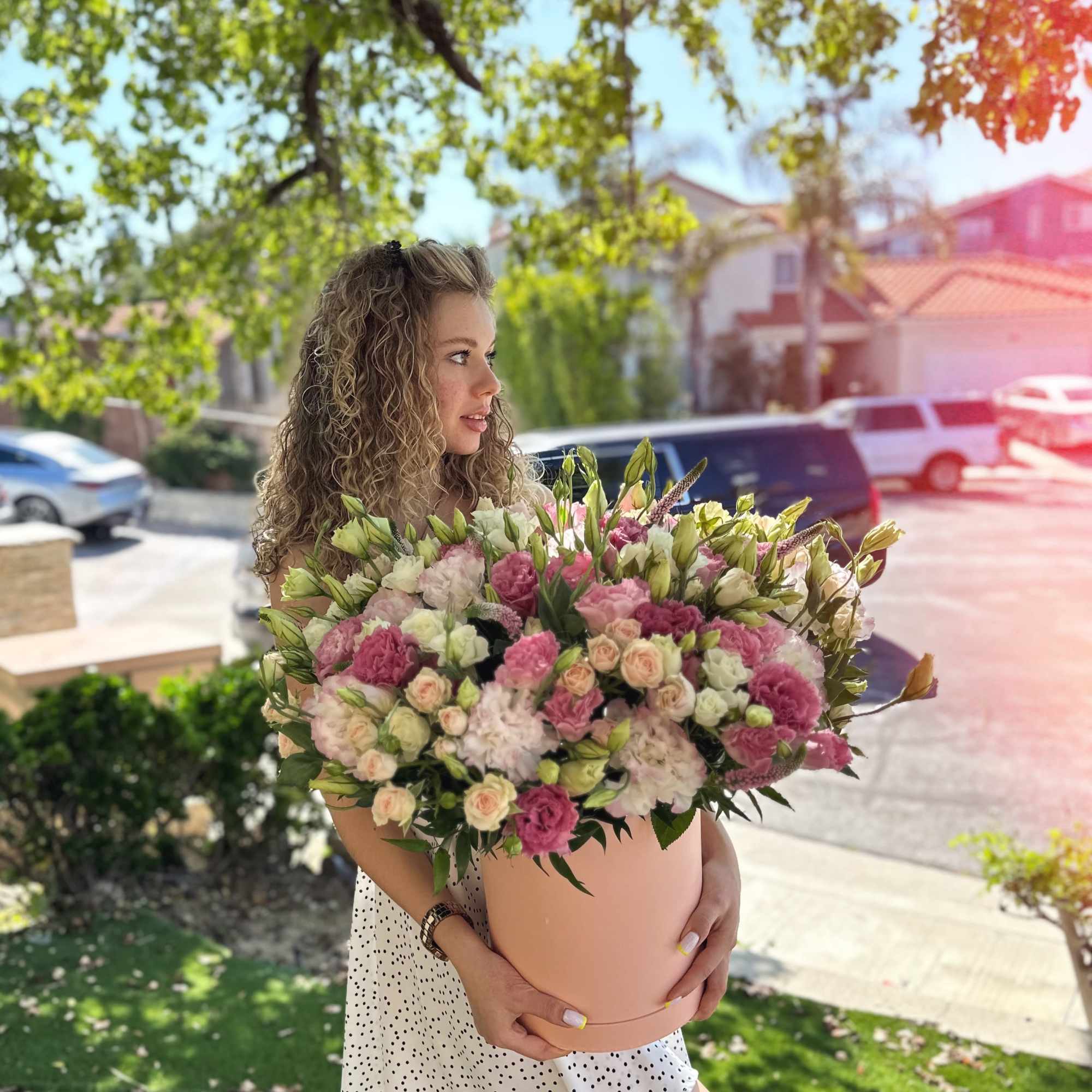 Woman holding a large pink and white flower arrangement in a round box