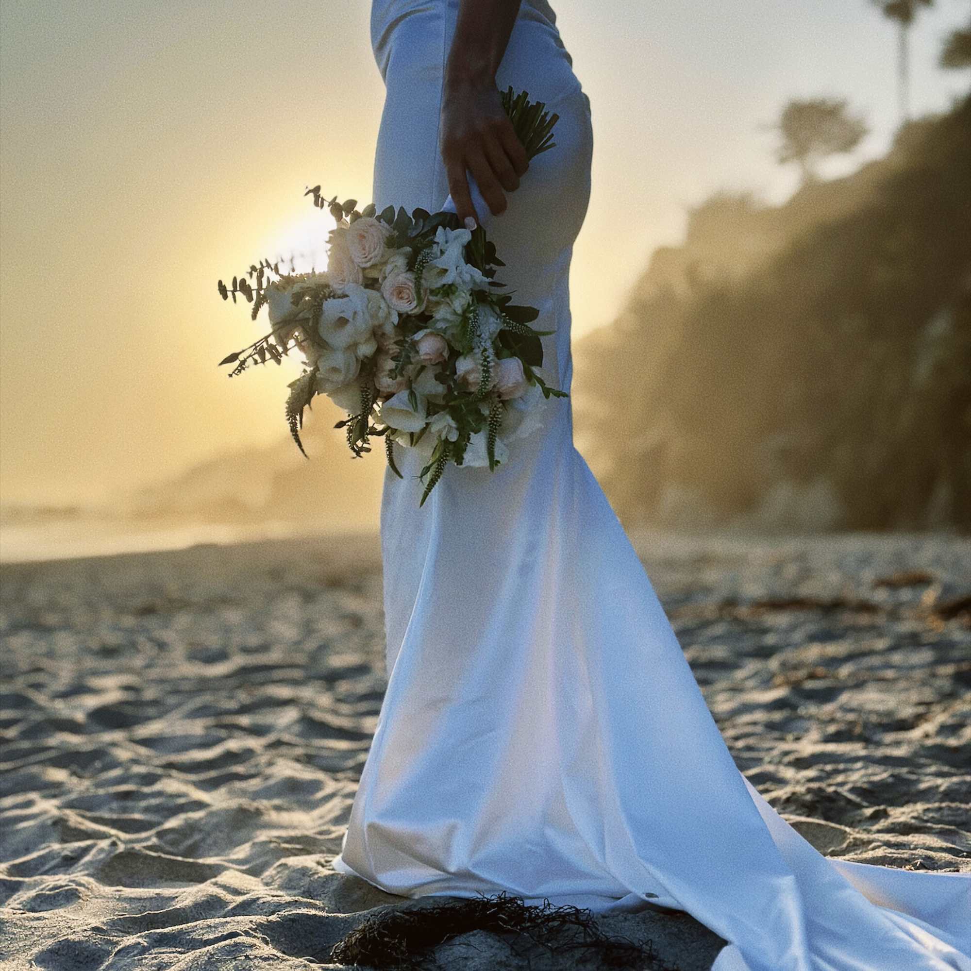 Bride holding a white and blush bouquet on a beach at sunset
