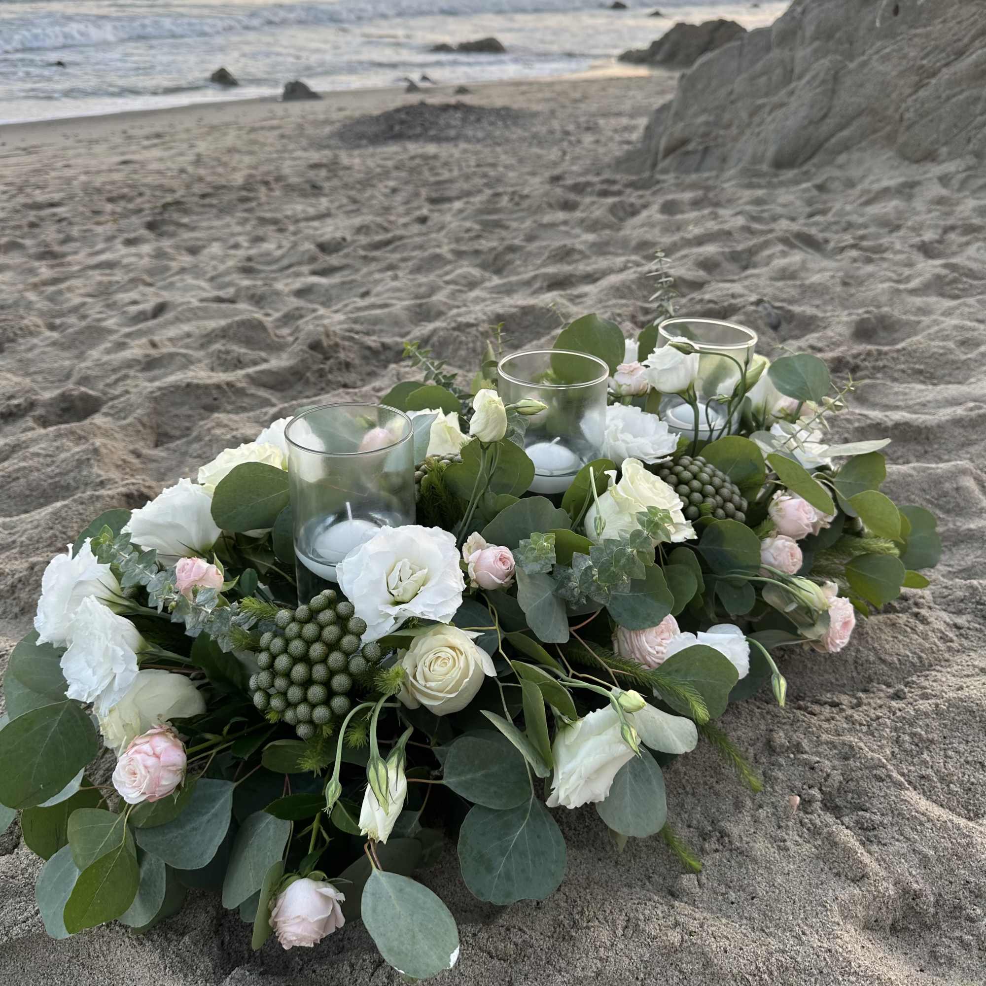 Low floral centerpiece with white roses and candles on the sand