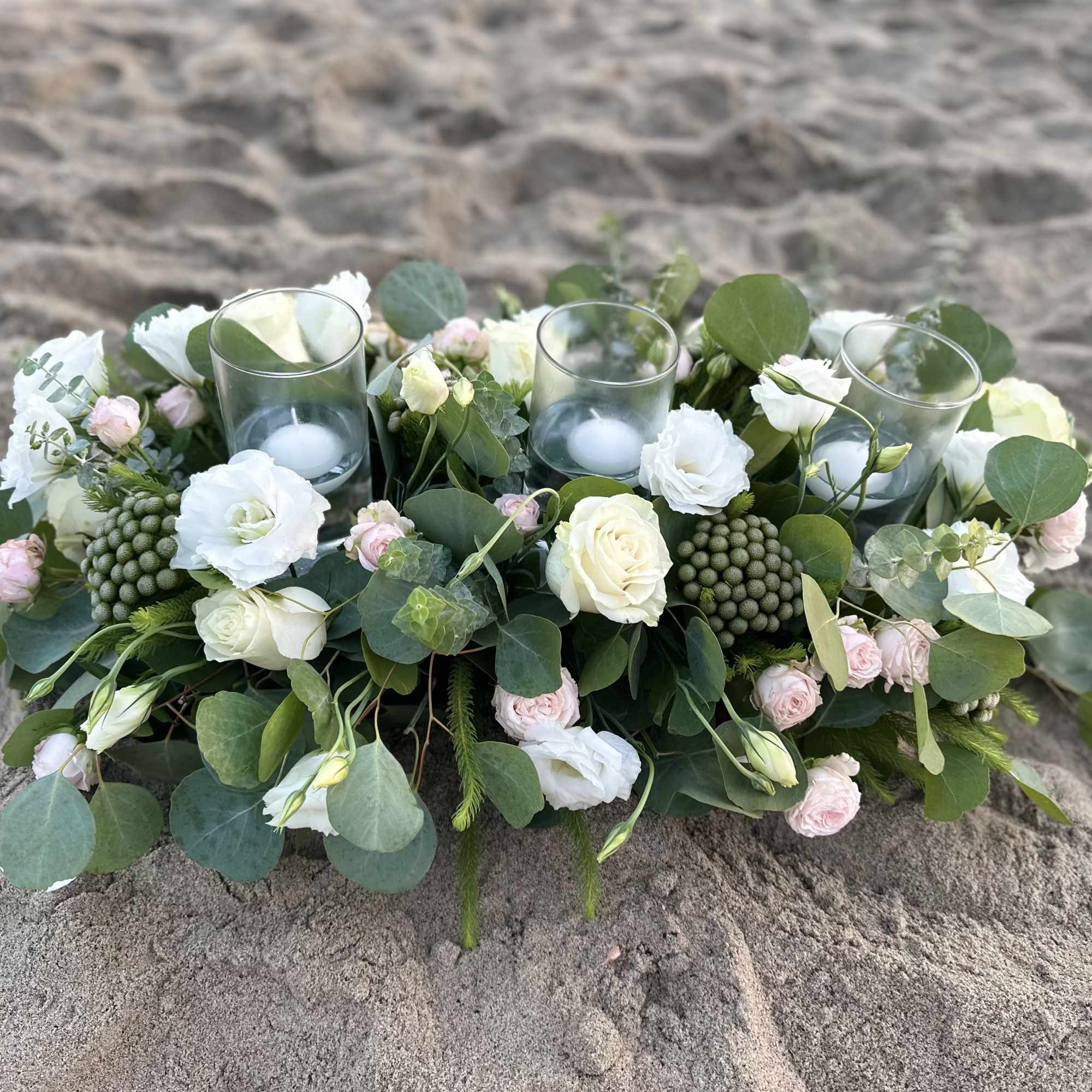 Low floral centerpiece with white and blush blooms around glass candle holders
