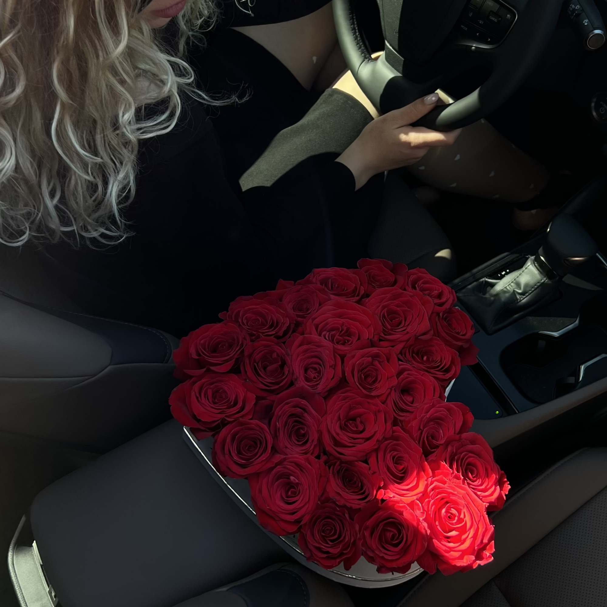 Woman in a car holding a heart-shaped bouquet of red roses