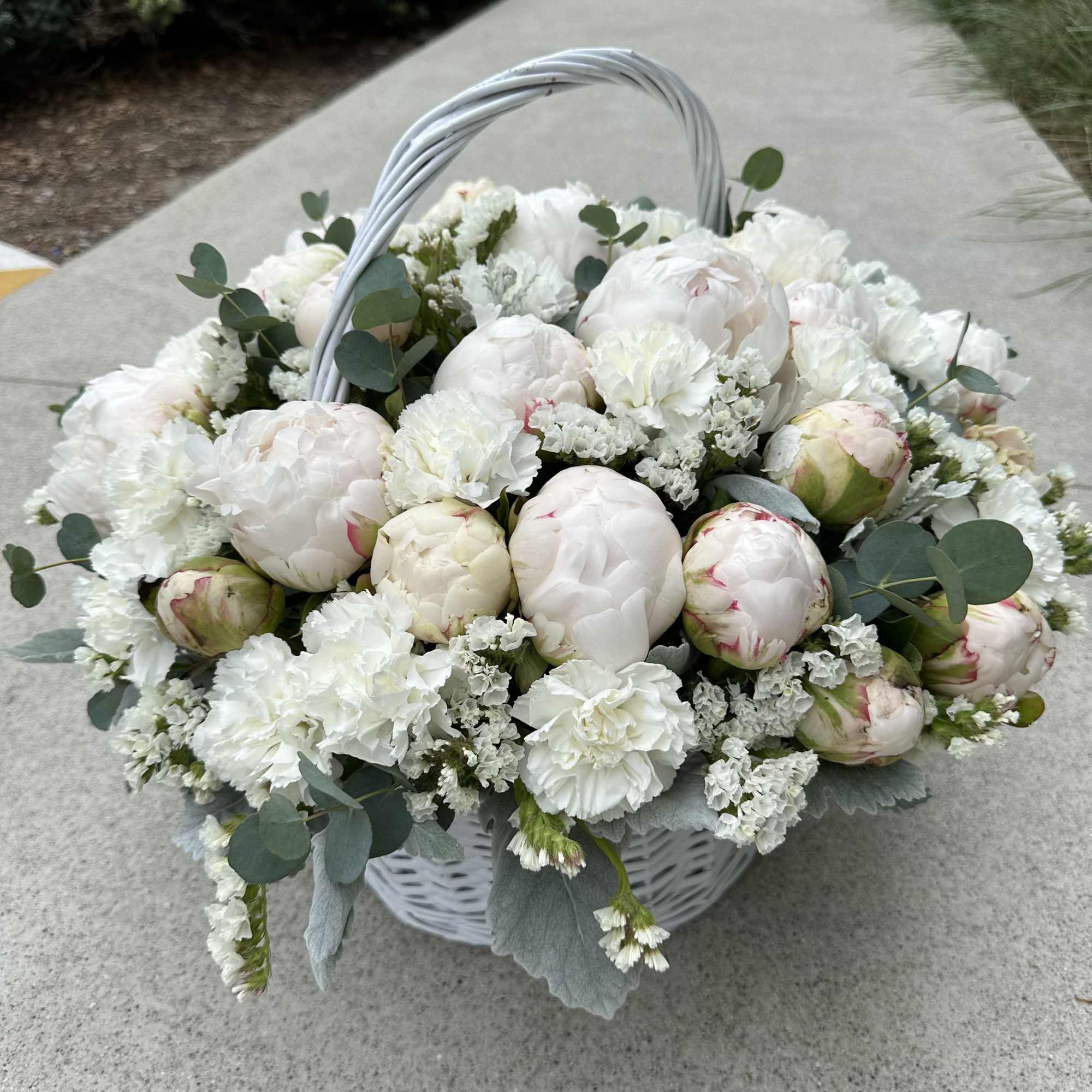 White peony basket arrangement with eucalyptus and a woven handle