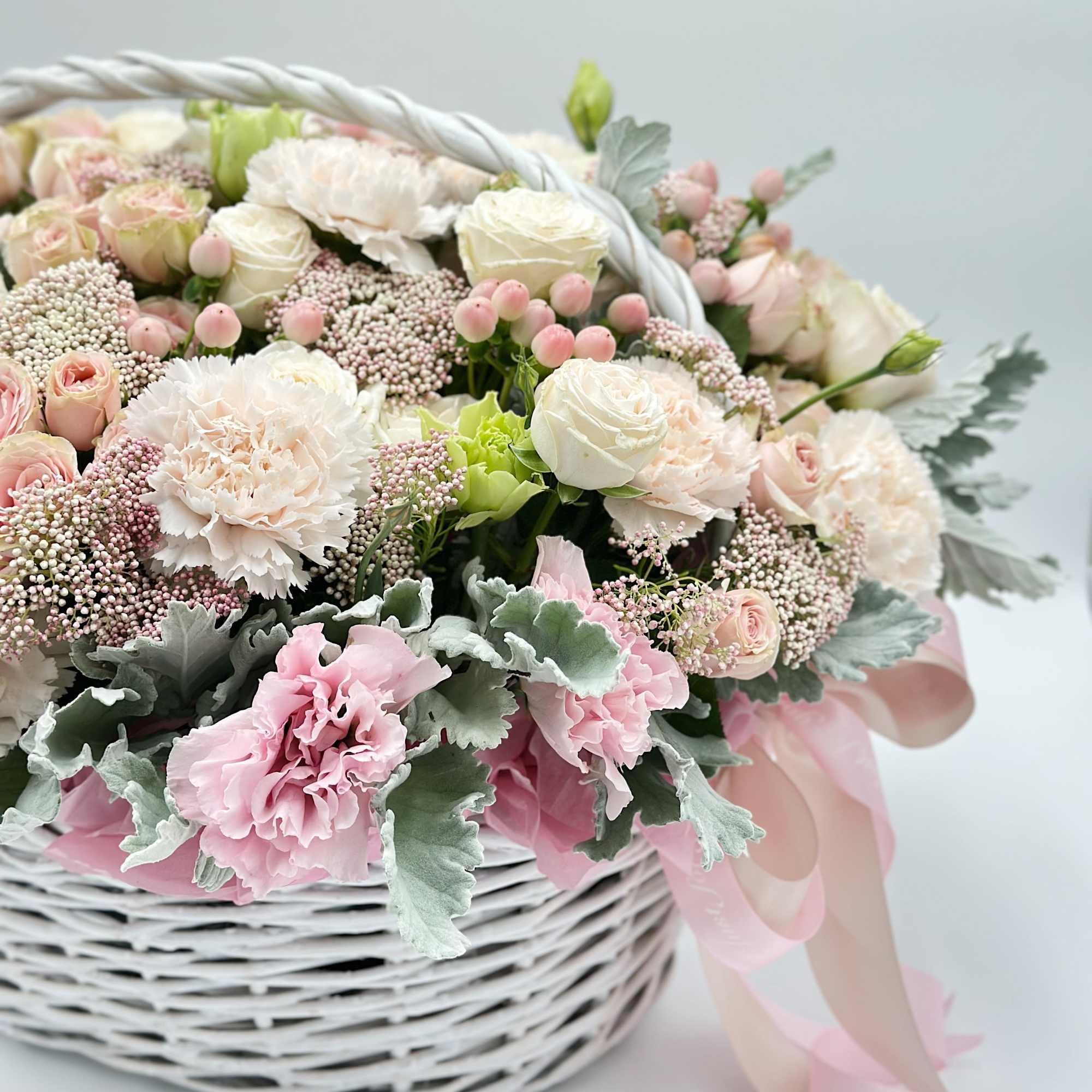 Pastel flower arrangement in a white wicker basket with pink ribbon