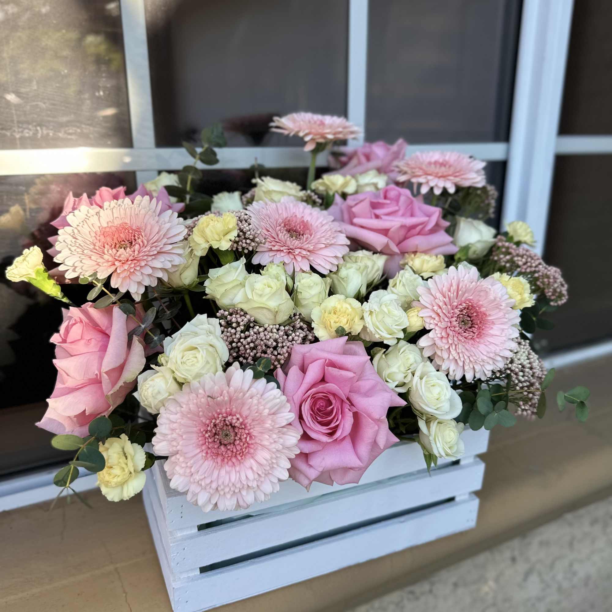 Pink roses and gerbera daisies arranged in a white wooden crate