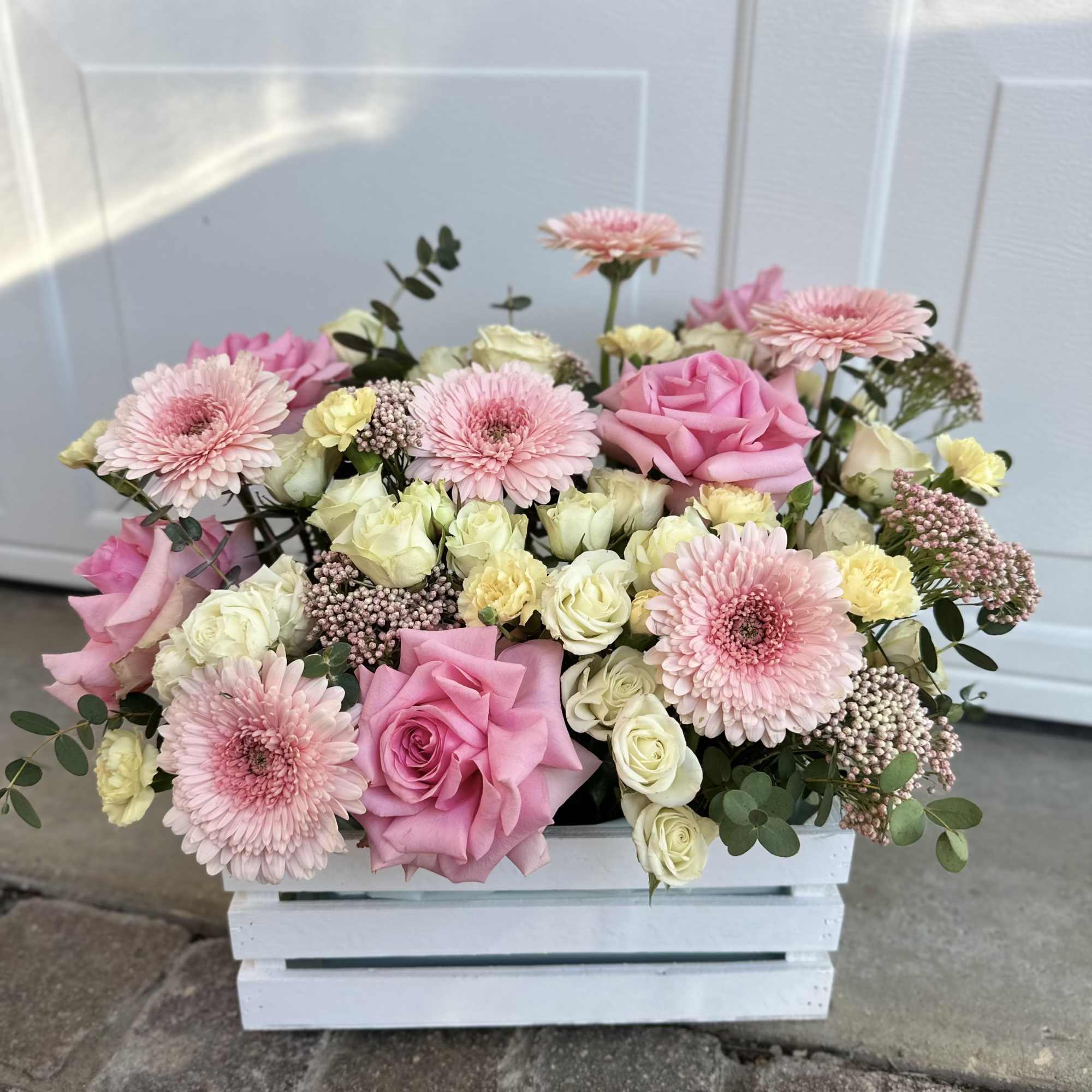 Pink and cream flower arrangement in a white wooden box